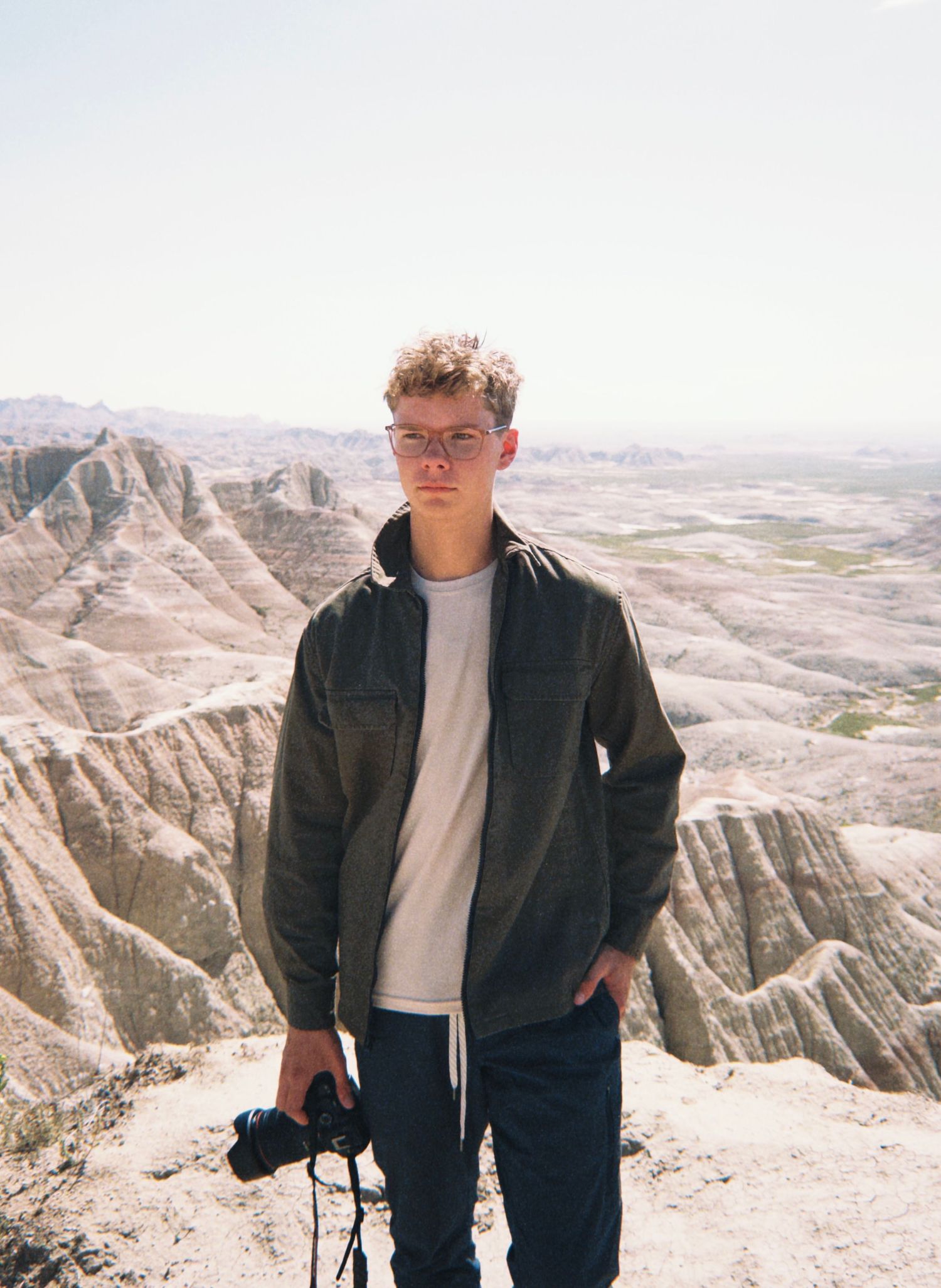 Young man with camera stands on rocky overlook at Badlands National Park, South Dakota.