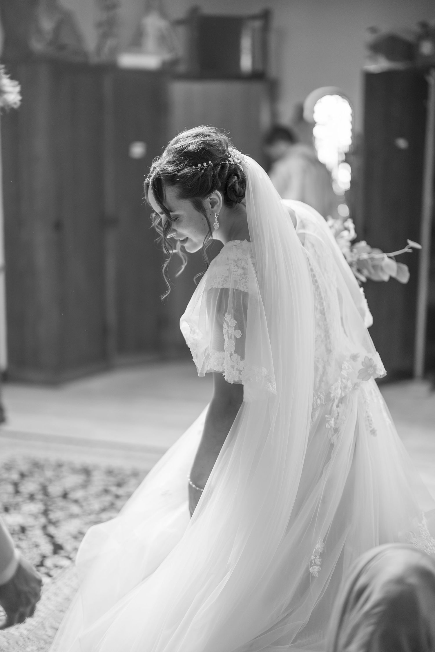 Black and white photo of a bride in a lace veil and wedding gown bowing gracefully during a church ceremony.