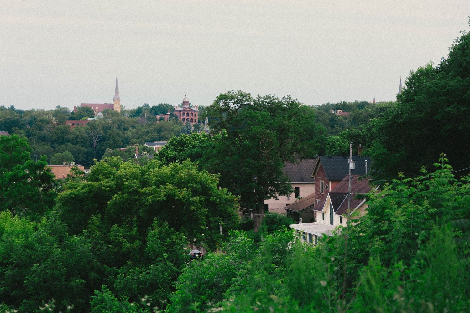 Aerial view of a lush green small town with historic church steeple and brick buildings nestled among dense trees.