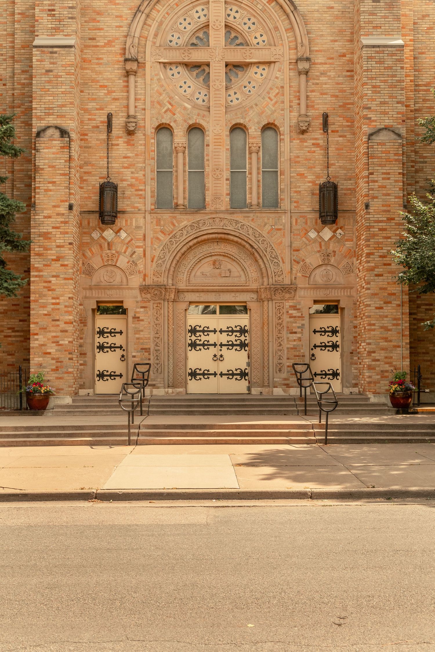 Classic brick Catholic church facade with ornate cross, arched doors, and decorative stonework.