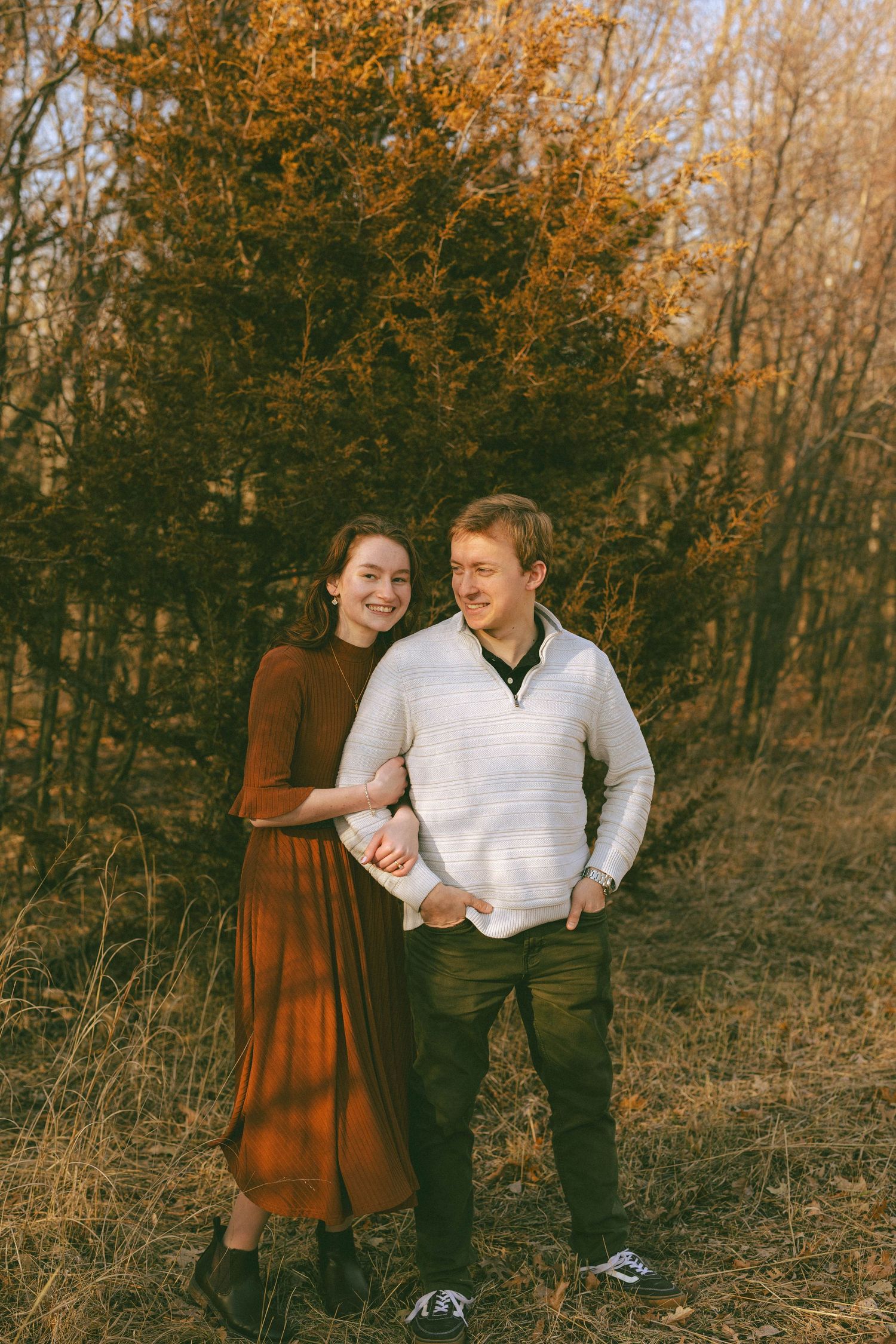 Happy couple standing together in an autumn landscape with golden foliage in the background.