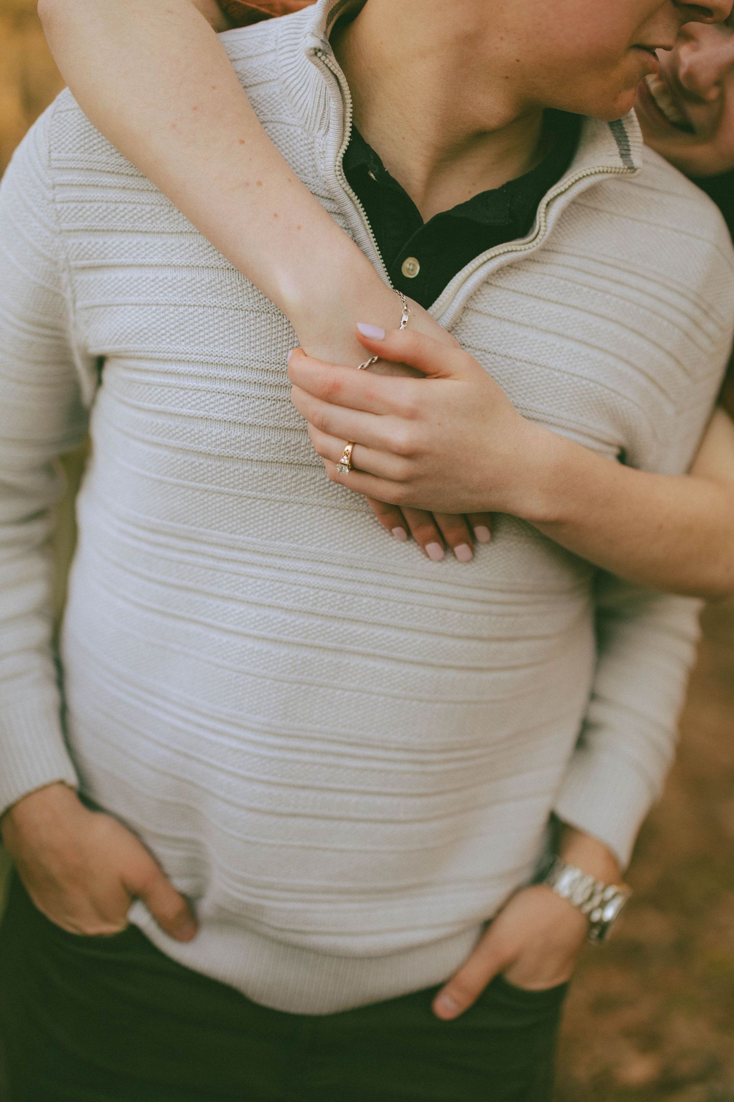 Close-up of a womans hands with an engagement ring embracing a man in a white knit sweater.