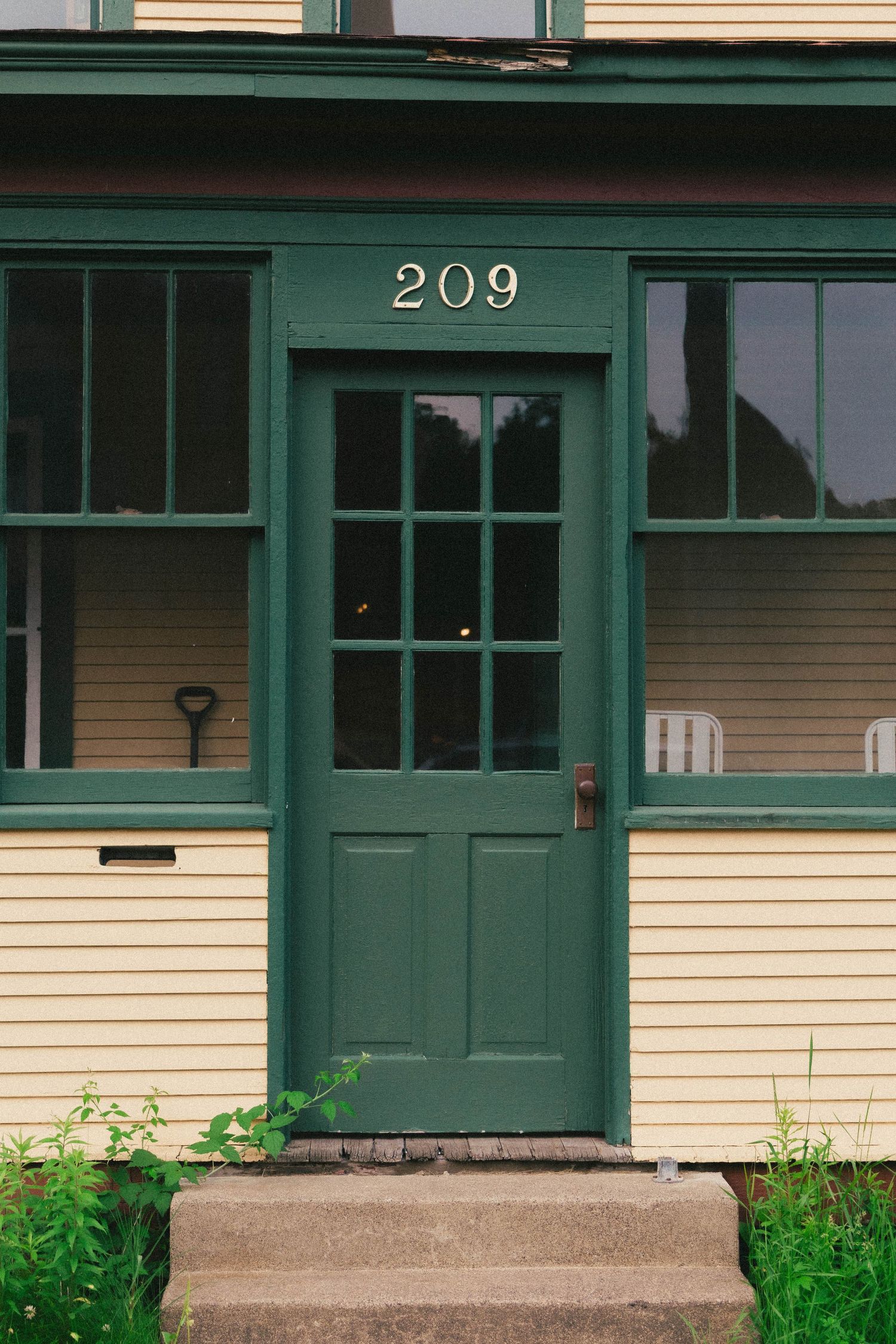 Green door numbered 209 on a yellow clapboard house with large windows and concrete steps.