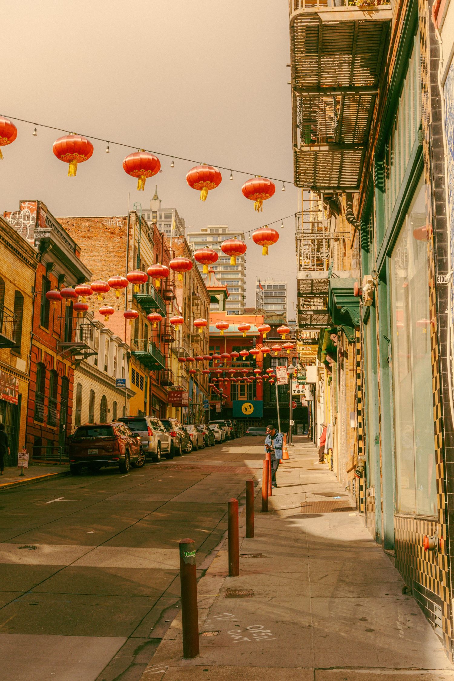 Colorful red Chinese lanterns strung above a quiet Chinatown street lined with historic buildings.
