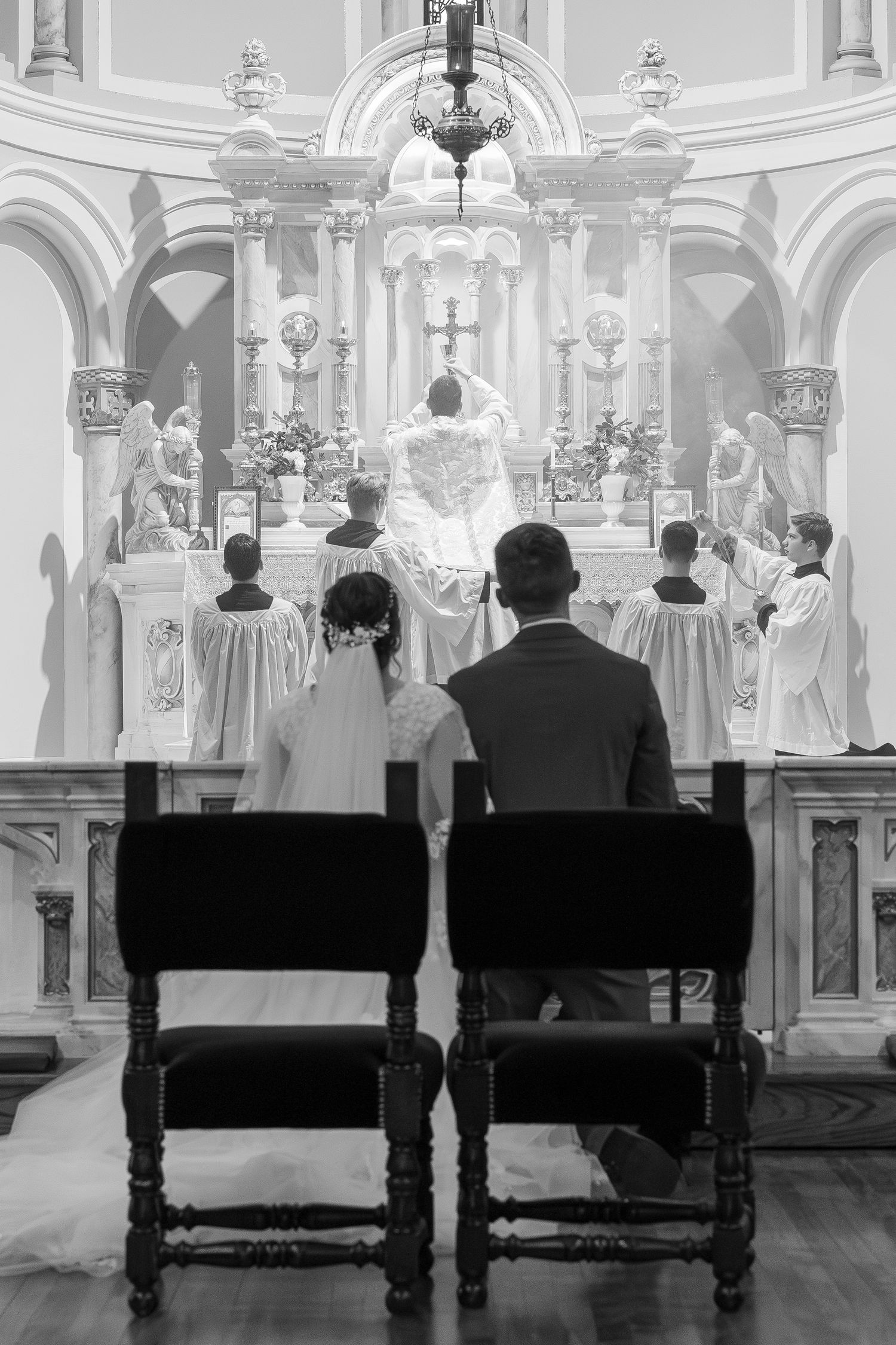 Black and white photo of bride and groom kneeling before the altar during a Catholic wedding Mass.