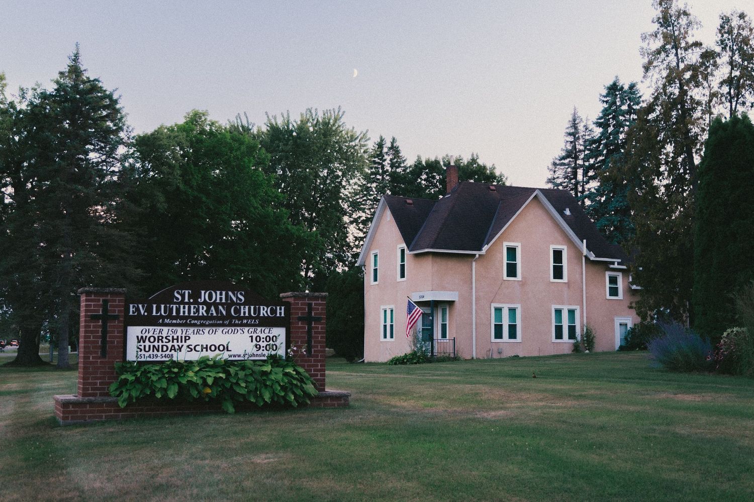 St. Johns Evangelical Lutheran Church pink building with green trees and sign on a quiet rural property.