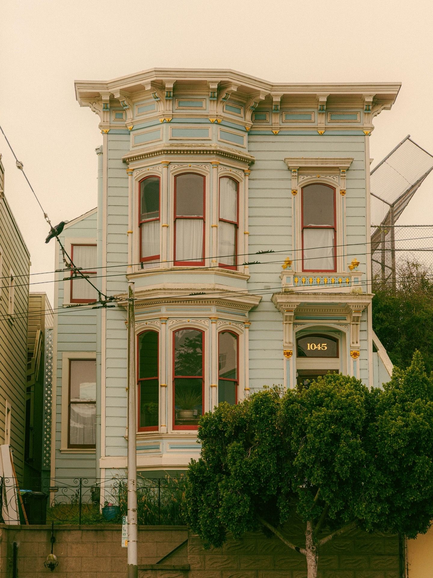 Victorian house with light blue exterior, red trim, and bay windows at address 1045 in San Francisco.