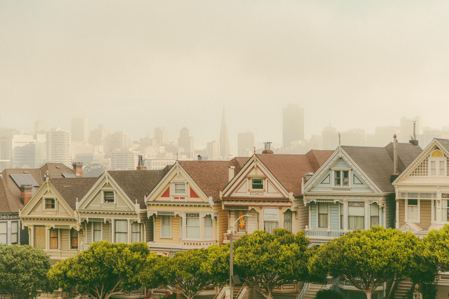 The iconic Painted Ladies Victorian row houses in San Francisco with the misty downtown skyline rising behind them.