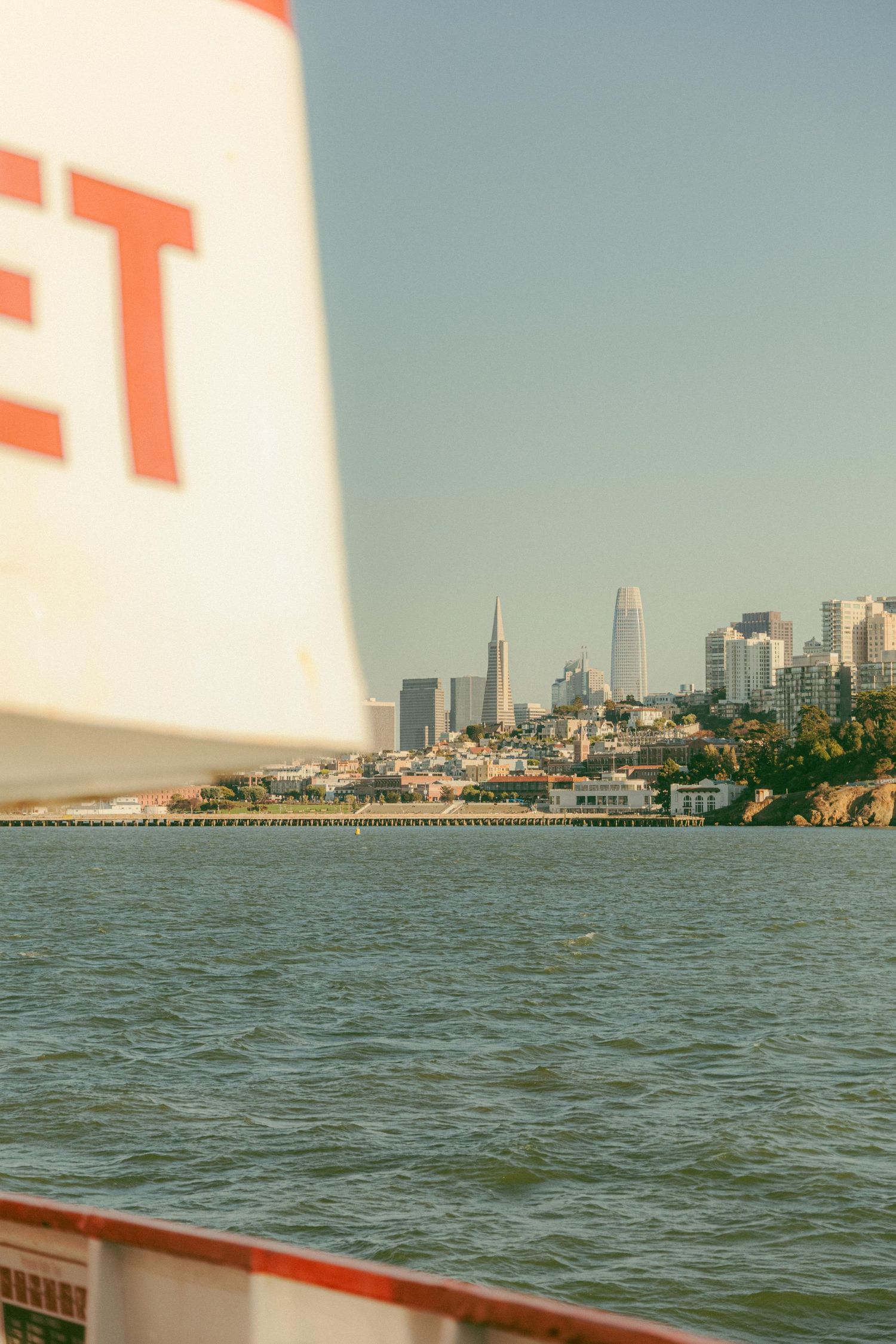 San Francisco skyline with Transamerica Pyramid viewed from a boat with a partial sail visible in foreground.