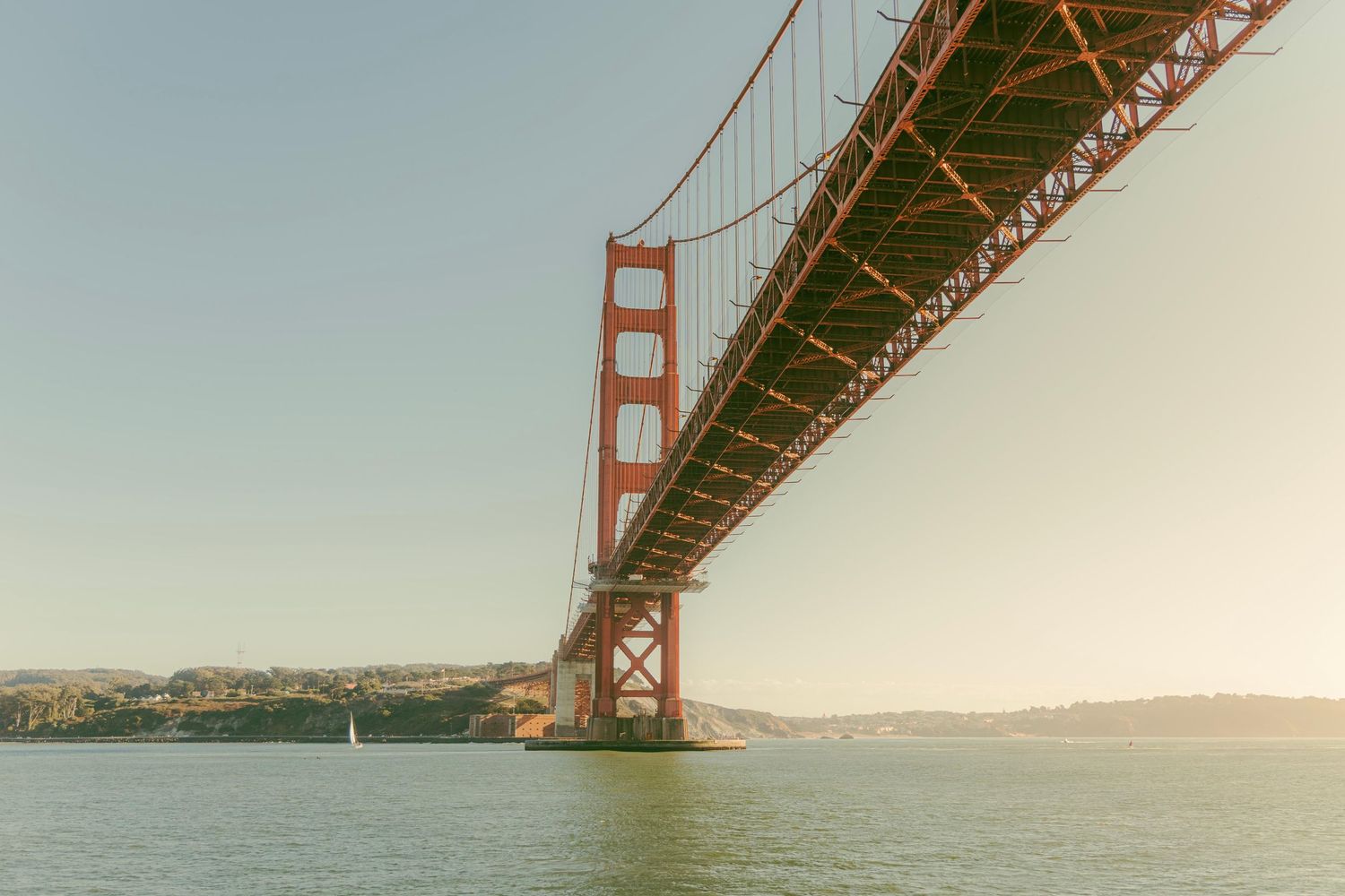 Golden Gate Bridge iconic red suspension structure viewed from below over San Francisco Bay at sunset.