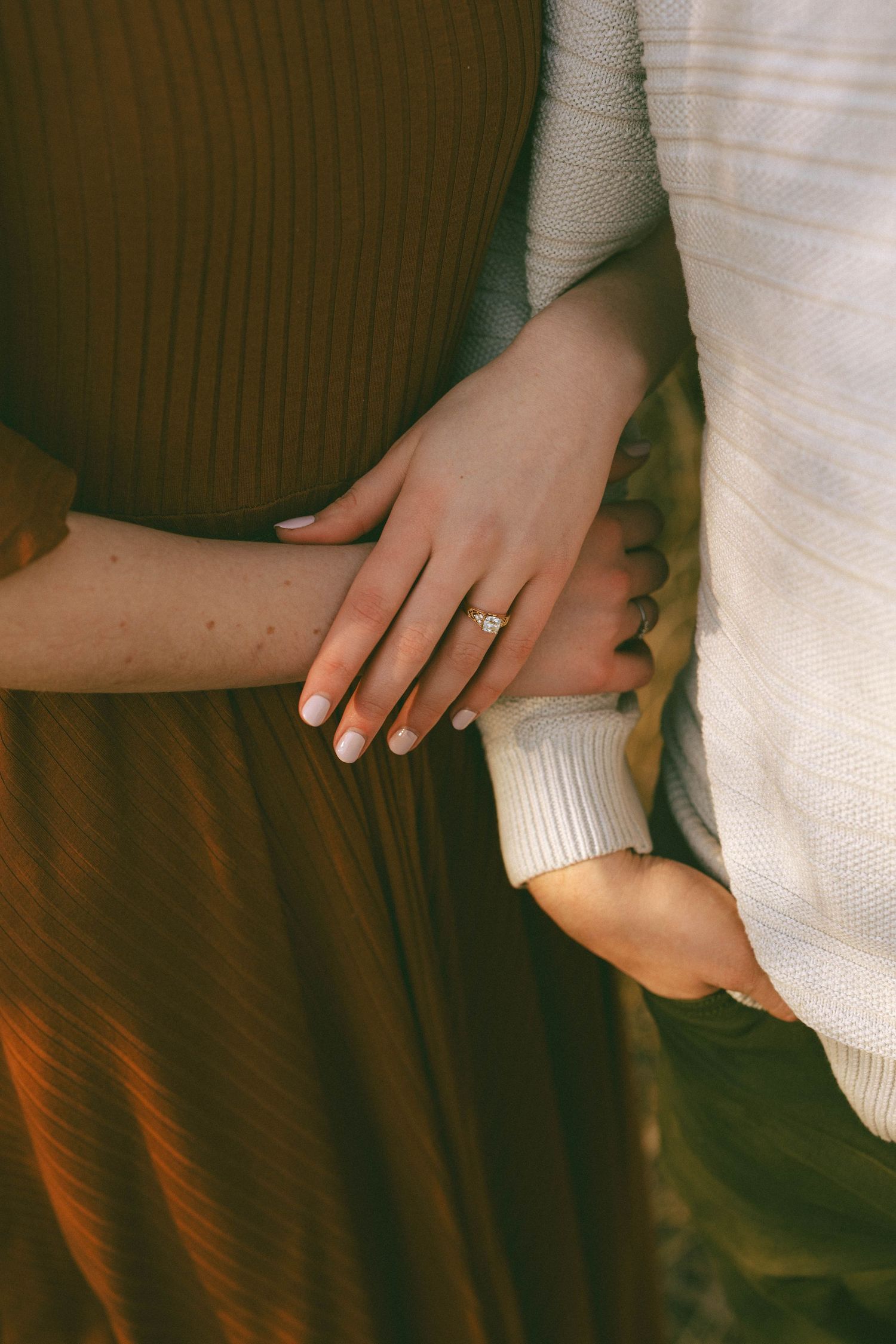 Close-up of a womans hand wearing an engagement ring resting on a rust-colored dress.