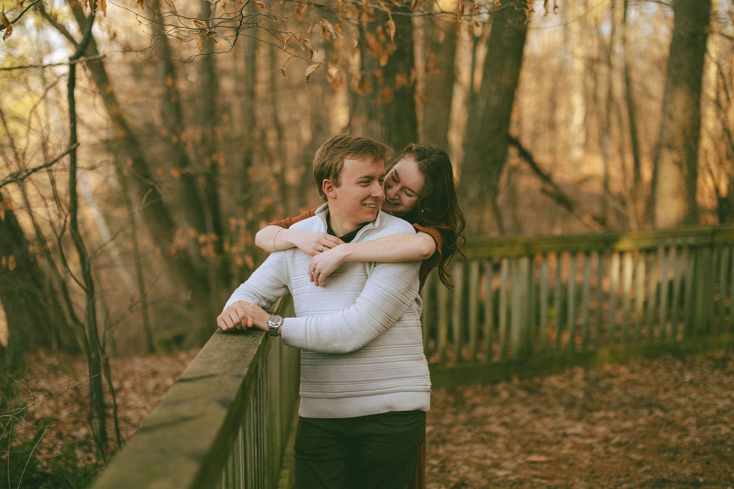 Couple embracing on a wooden bridge in an autumn forest, sharing a romantic moment among golden fallen leaves.