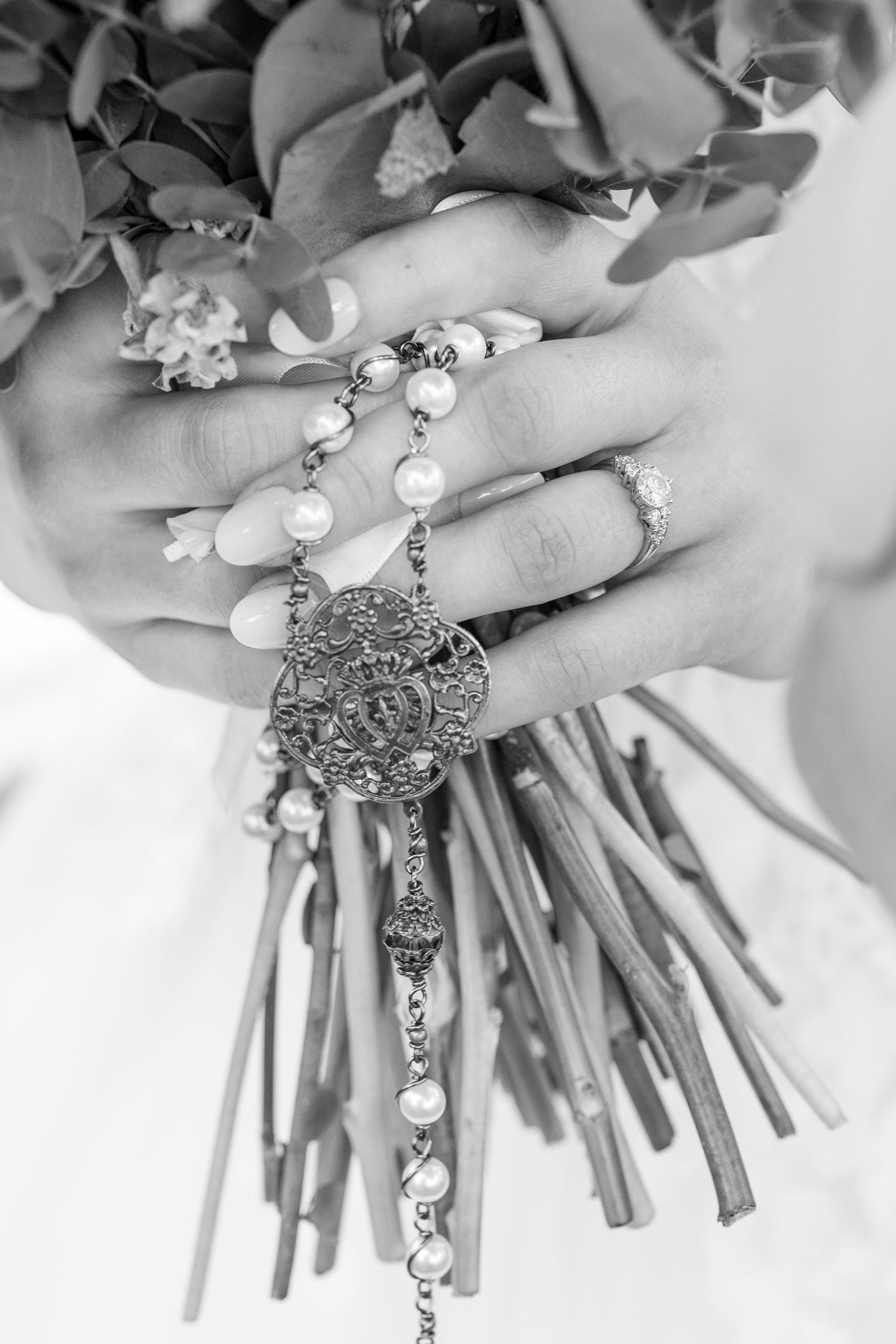 Black and white close-up of a bride holding a bouquet with a pearl rosary draped over her hand.