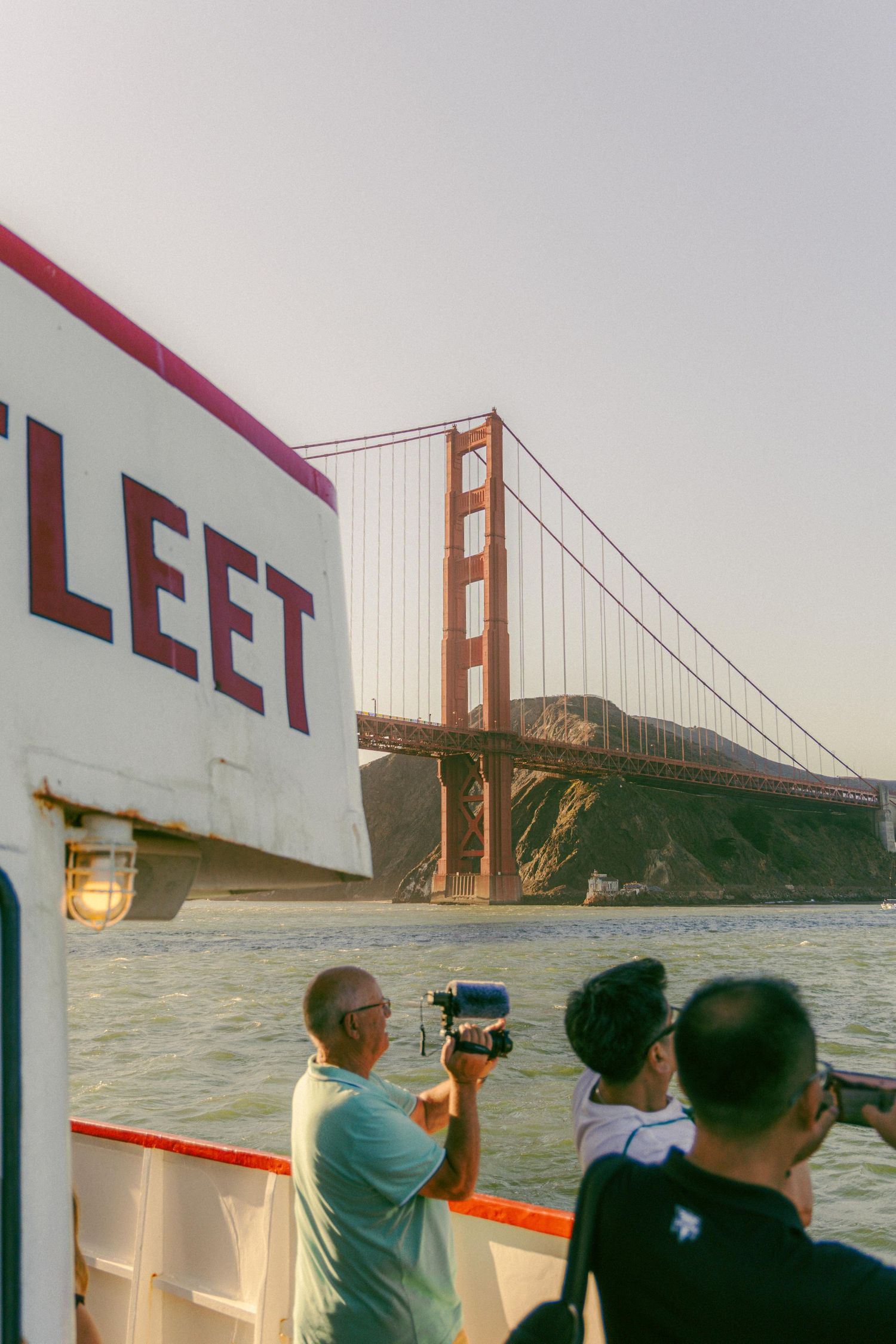 Tourists photographing the iconic Golden Gate Bridge from the deck of a Red and White Fleet ferry boat.