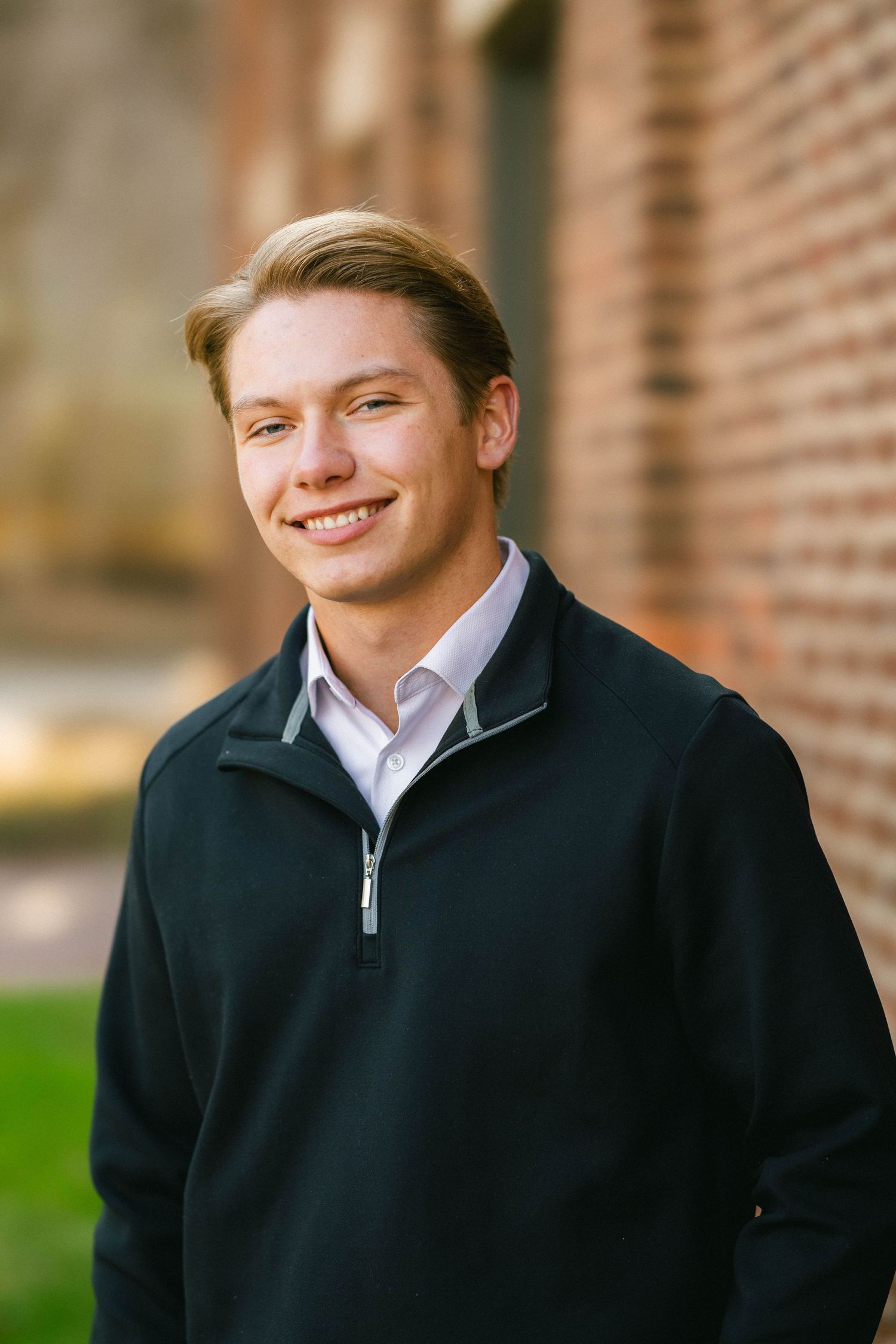 Senior portrait of a smiling young man against a background of rustic timeless brick wall in downtown historic Stillwater