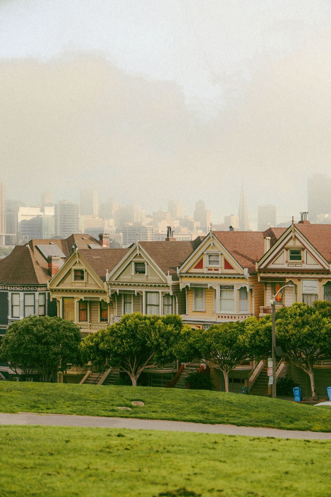 Famous Painted Ladies Victorian houses with San Francisco skyline visible through morning fog behind them.
