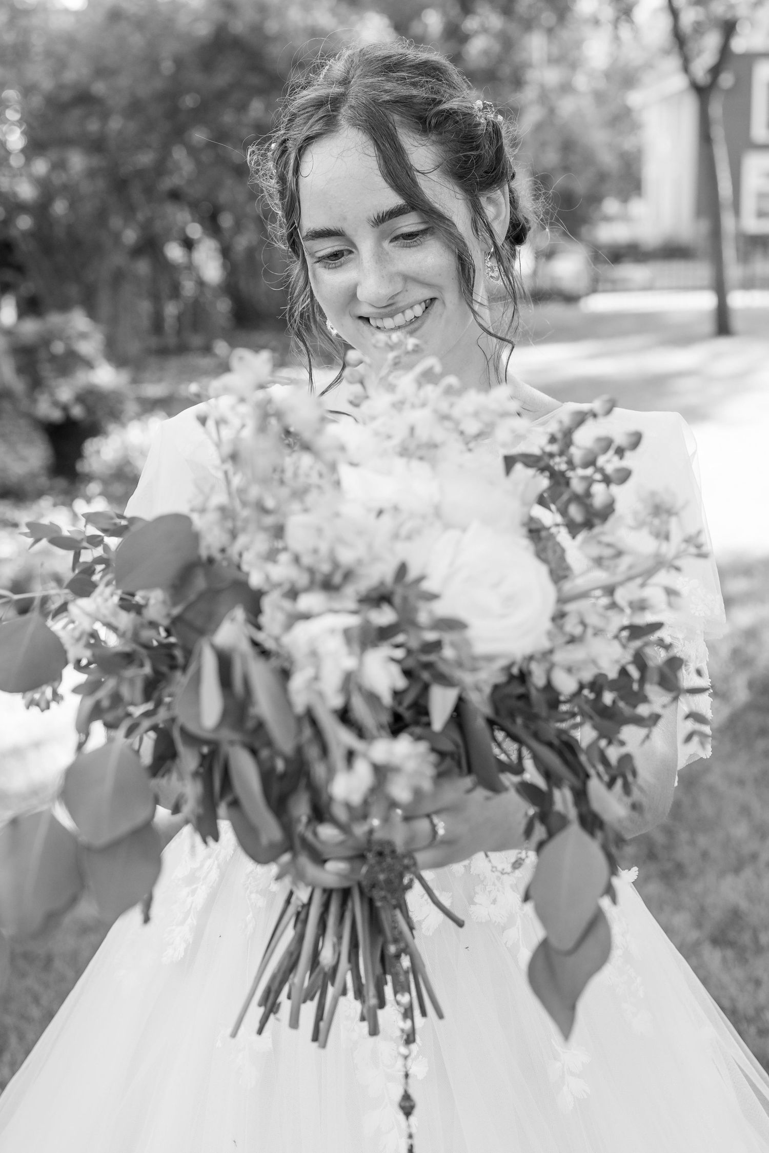 Black and white photo of a smiling bride holding a large floral bouquet outdoors.