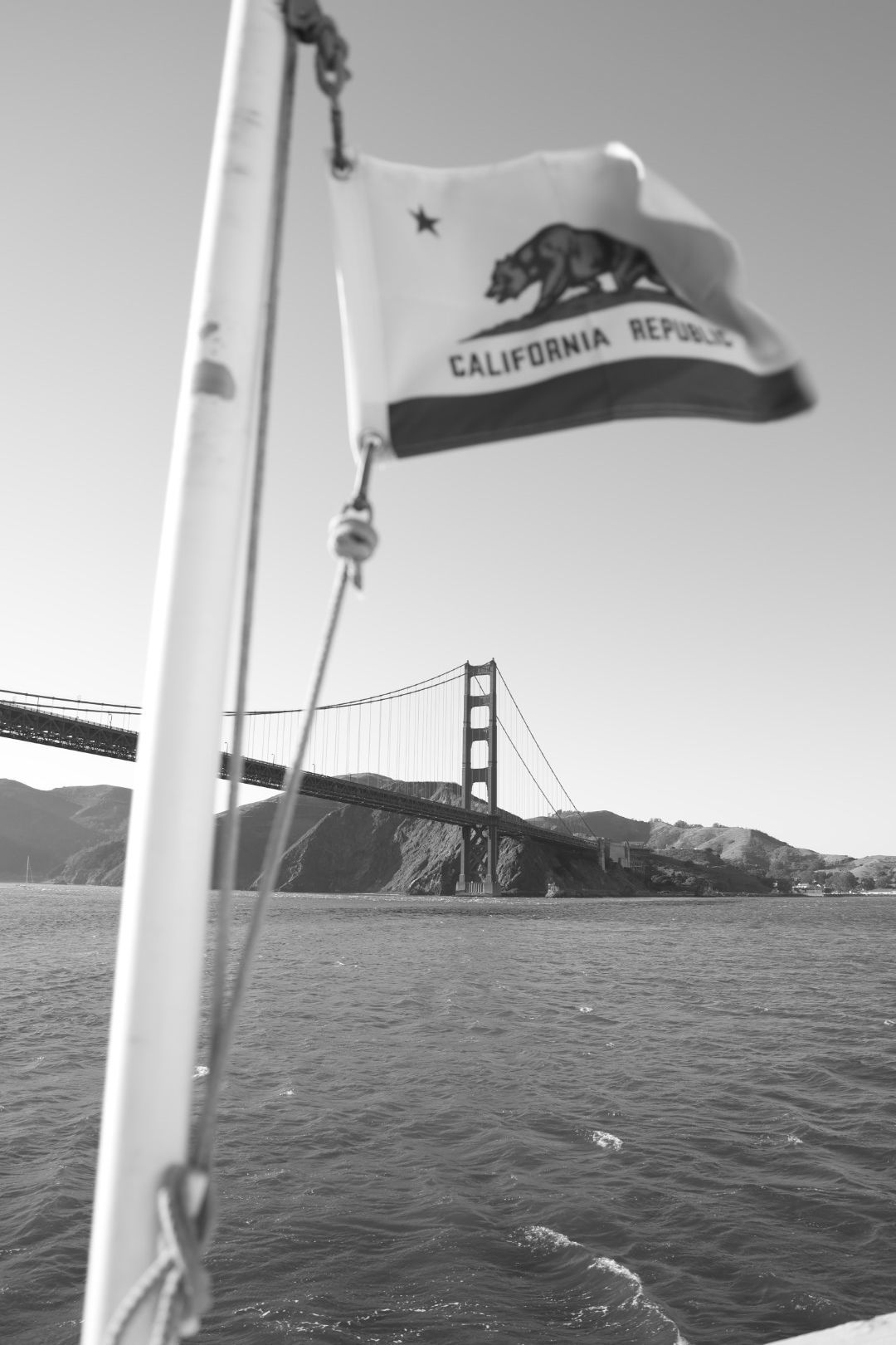 California Republic state flag flies on a boat with the Golden Gate Bridge visible in black and white.