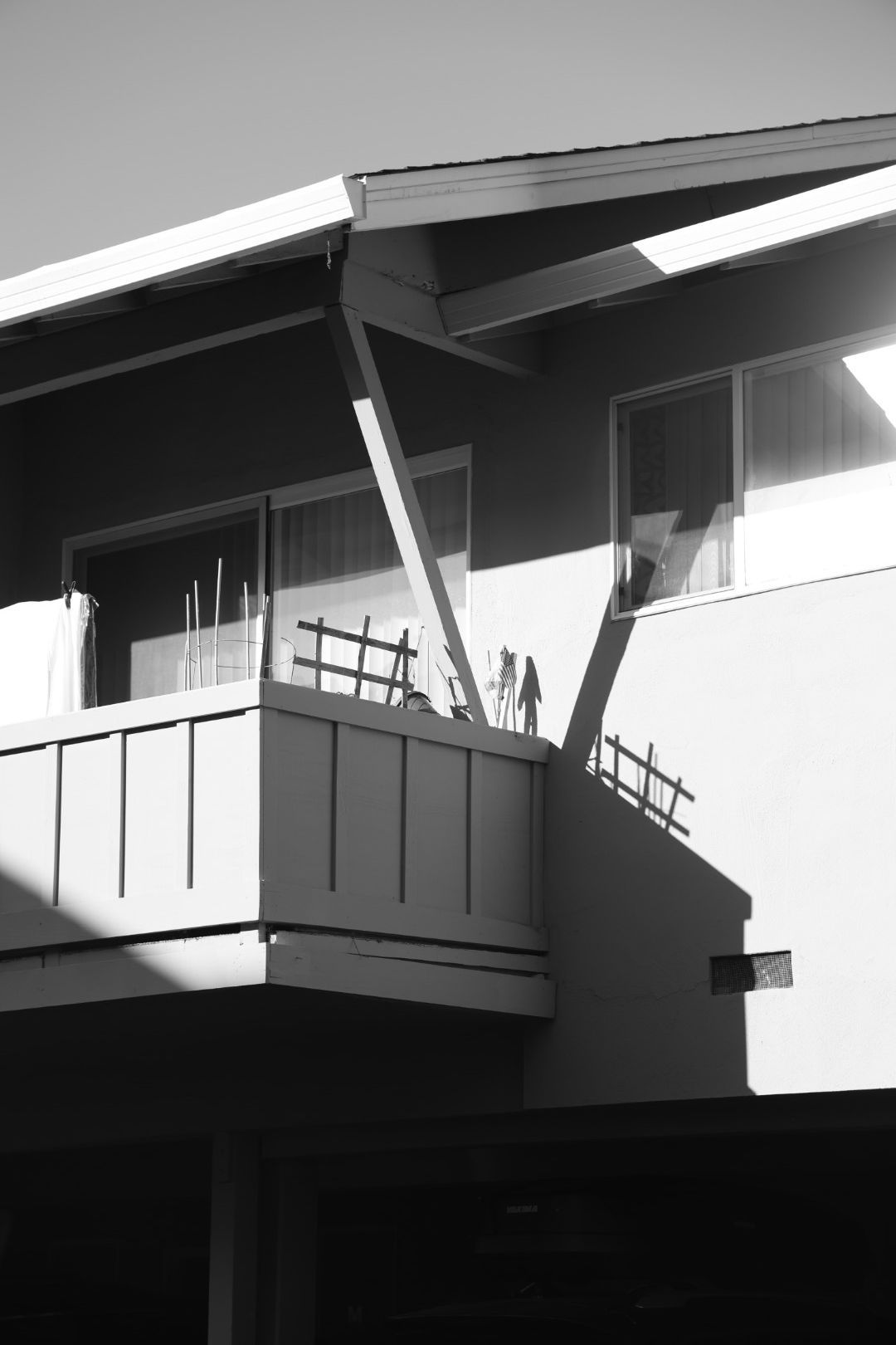 Black and white architectural photo of a modern building balcony with geometric shadows and clean lines.
