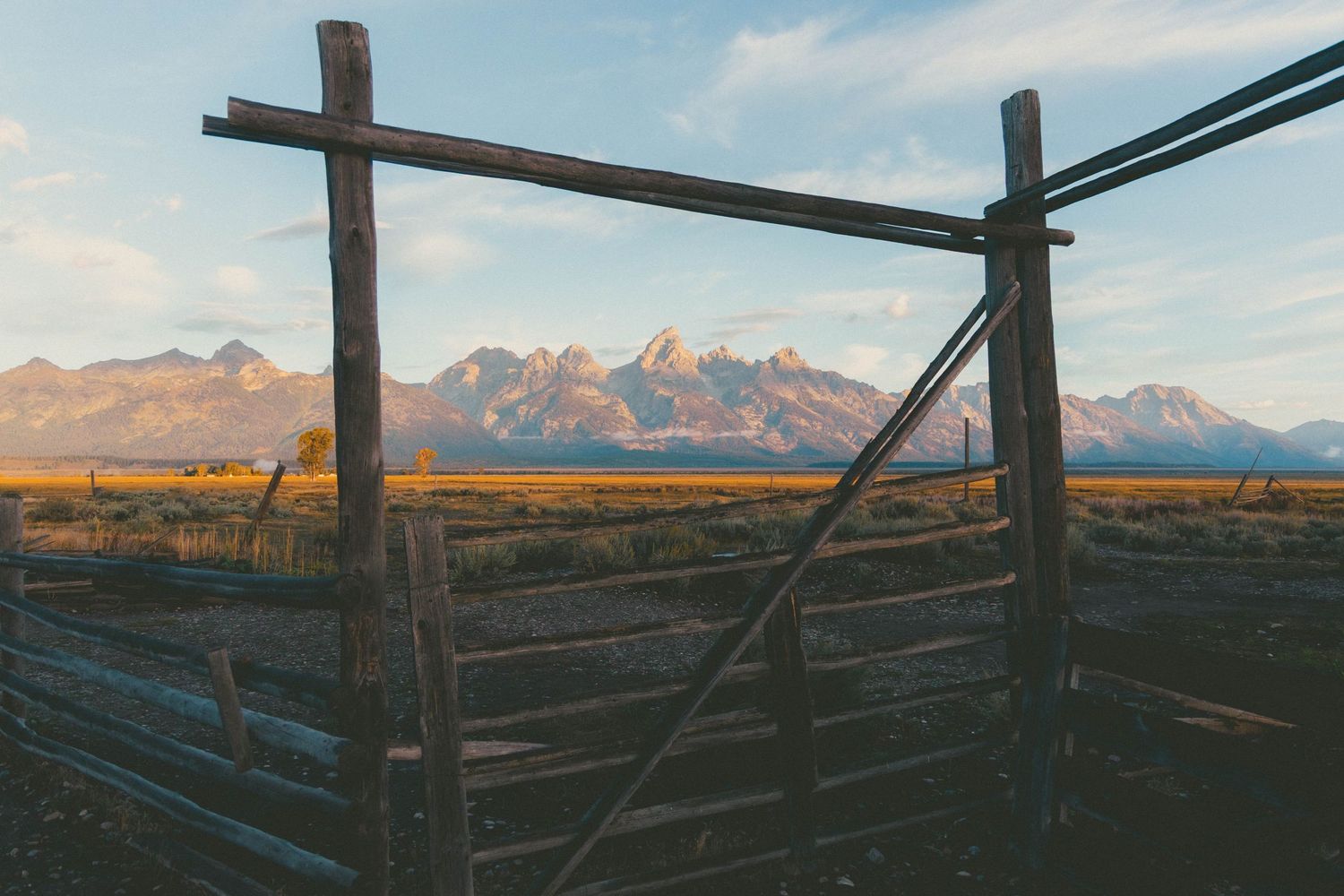 Rustic wooden fence gate with Grand Teton mountain range backdrop at golden hour in Wyoming.