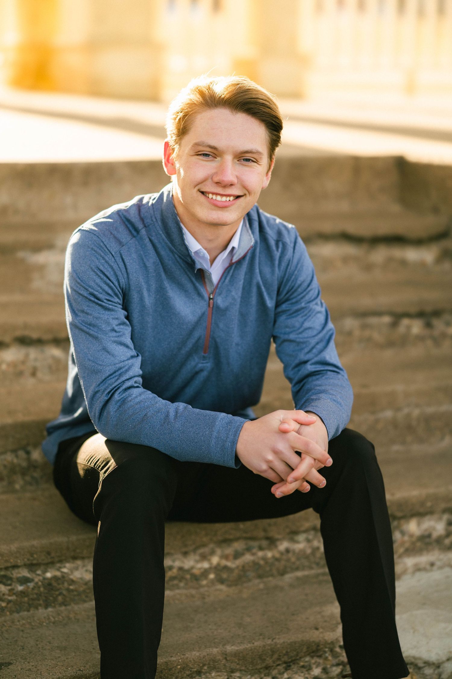 Senior portrait of a young man seated on rustic textured stairs smiling and happy in downtown Stillwater minnesota