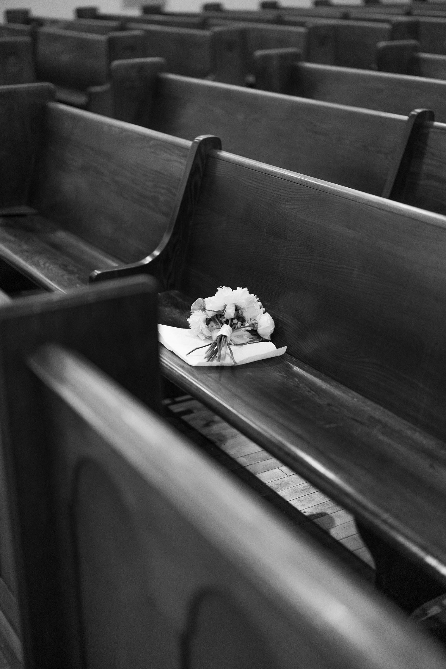 Black and white image of wooden church pews with a floral bouquet resting on one bench.