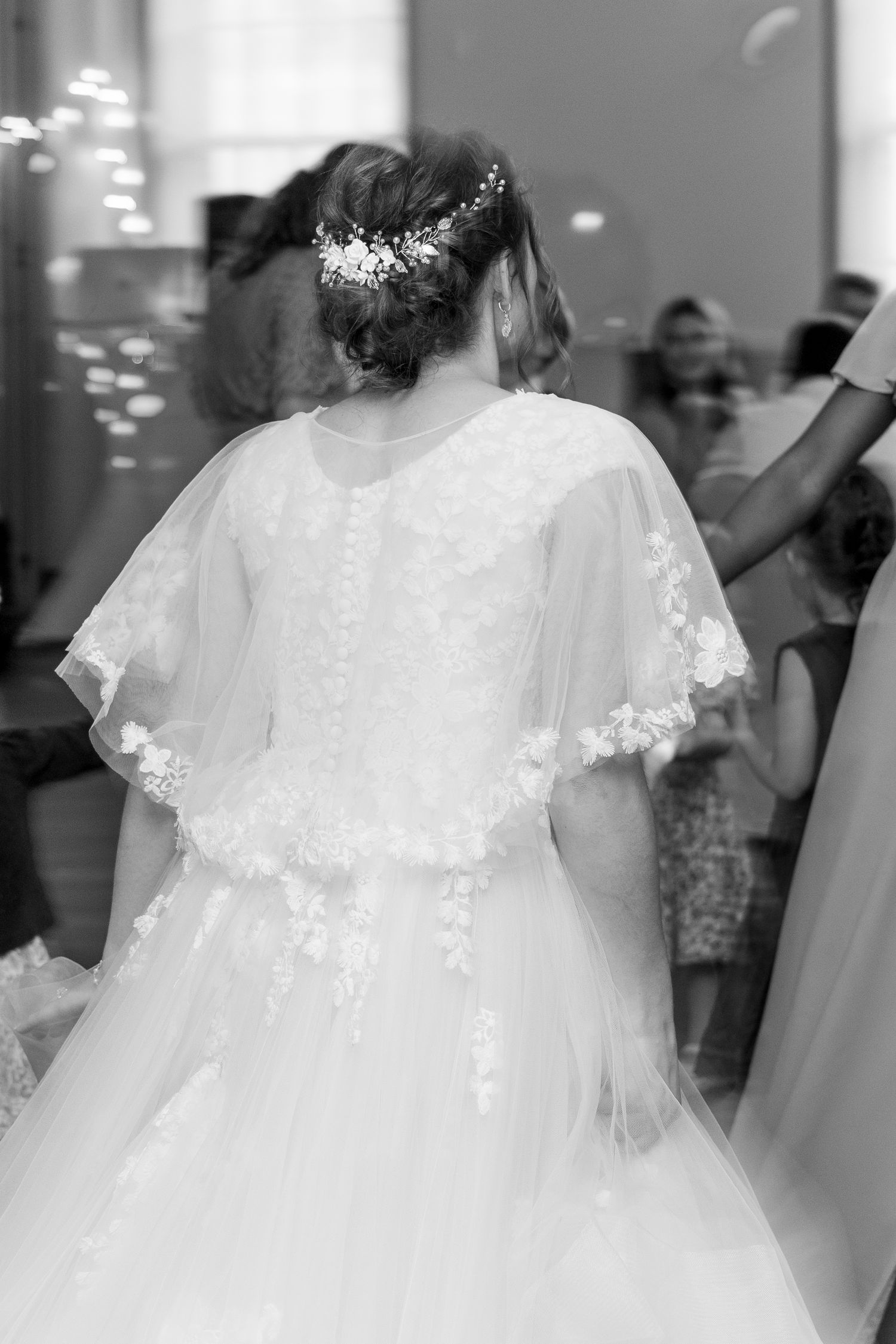 Black and white photo of a bride from behind in a lace wedding dress with floral hair accessories.