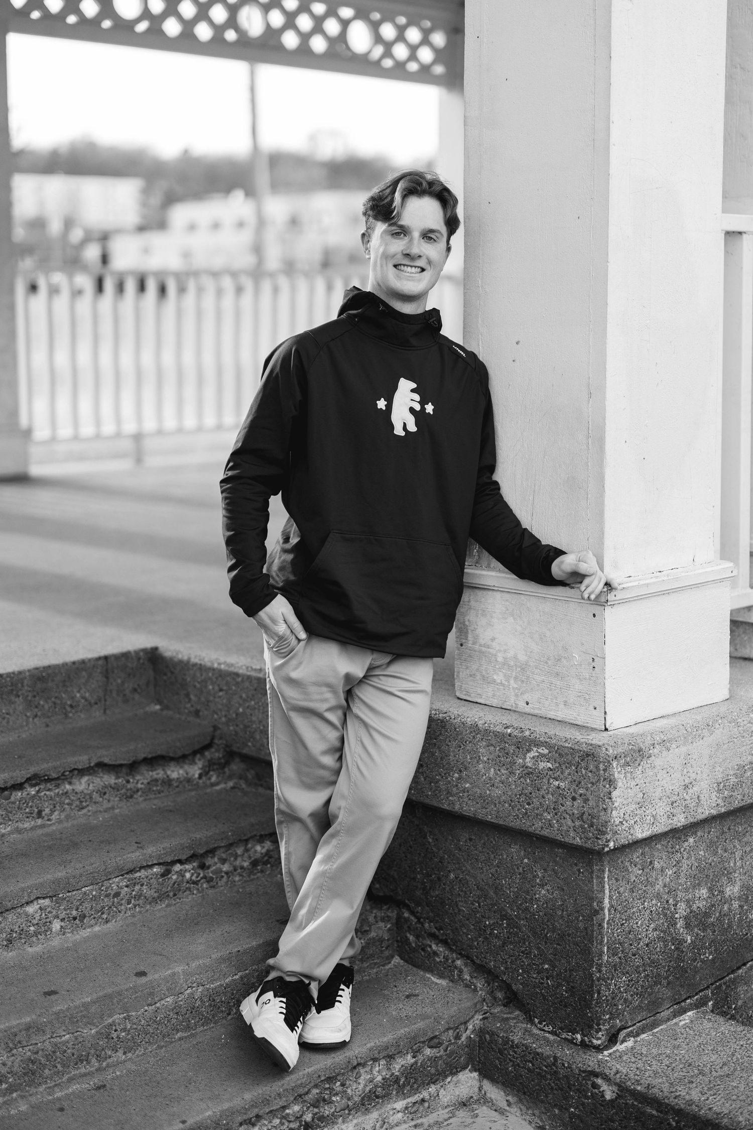 Young man in black hoodie smiling while leaning on column on steps.