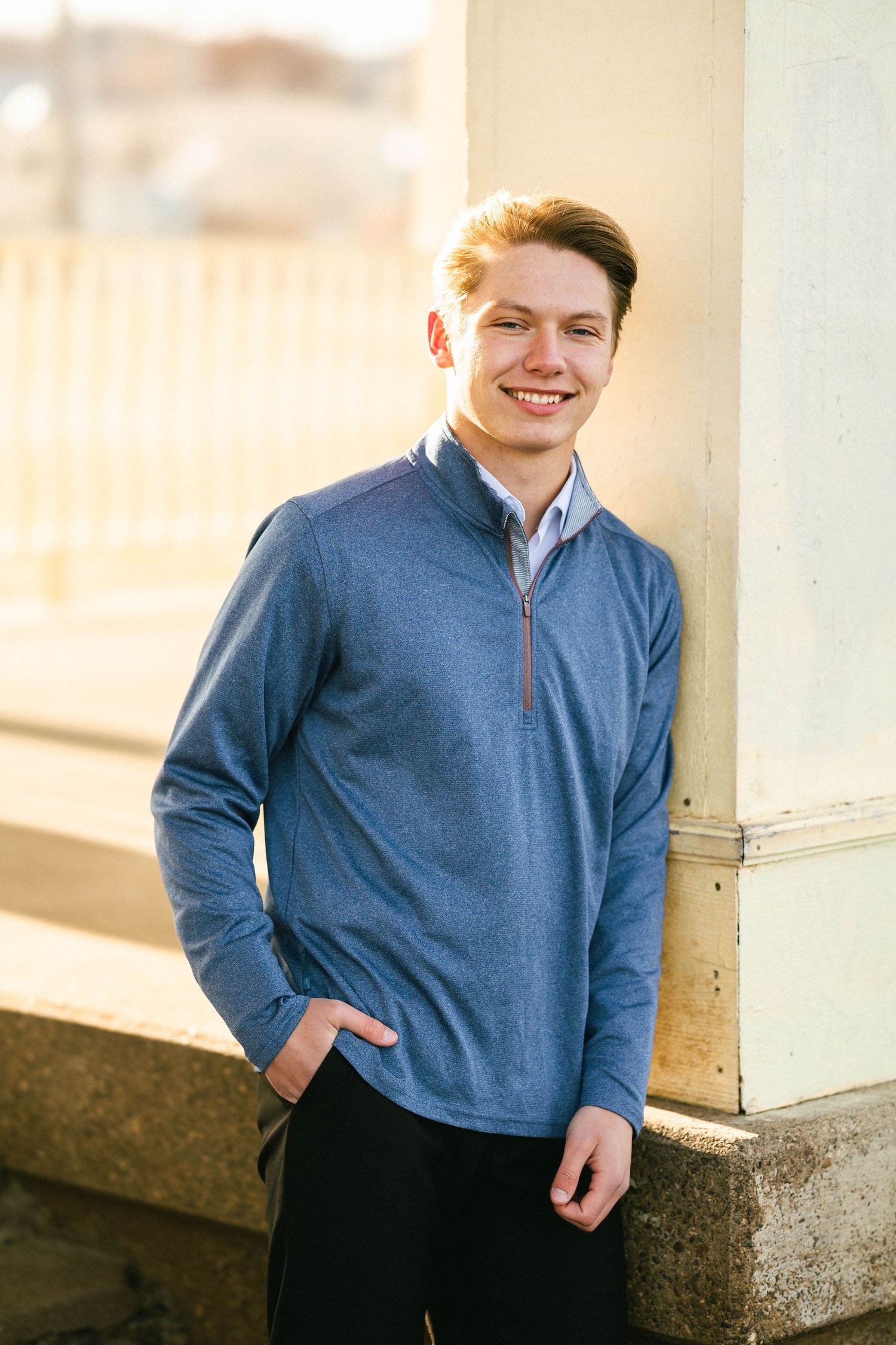 Senior portrait of a happy young man covered in sunshine standing against a white textured wall in Downtown Historic Stillwater minnesota