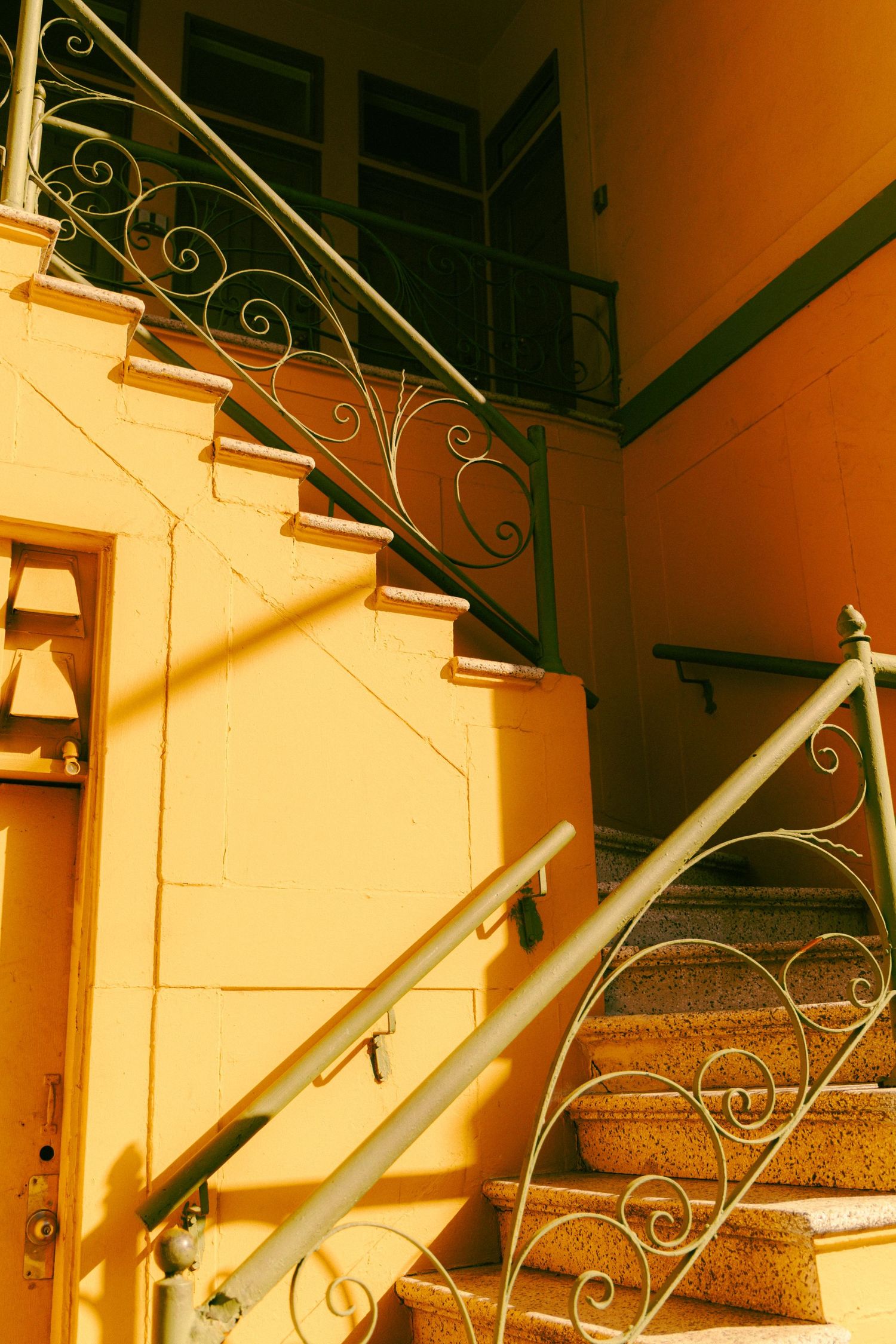 Ornate wrought iron staircase railing with spiral details on golden yellow exterior building wall in warm sunlight.