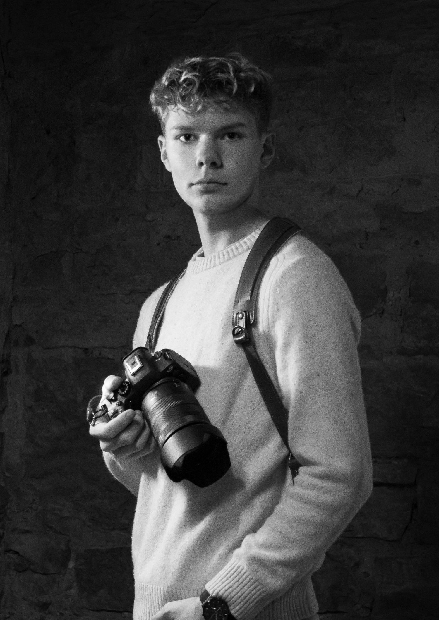 Young male photographer holding a DSLR camera with leather harness strap, black and white studio portrait.