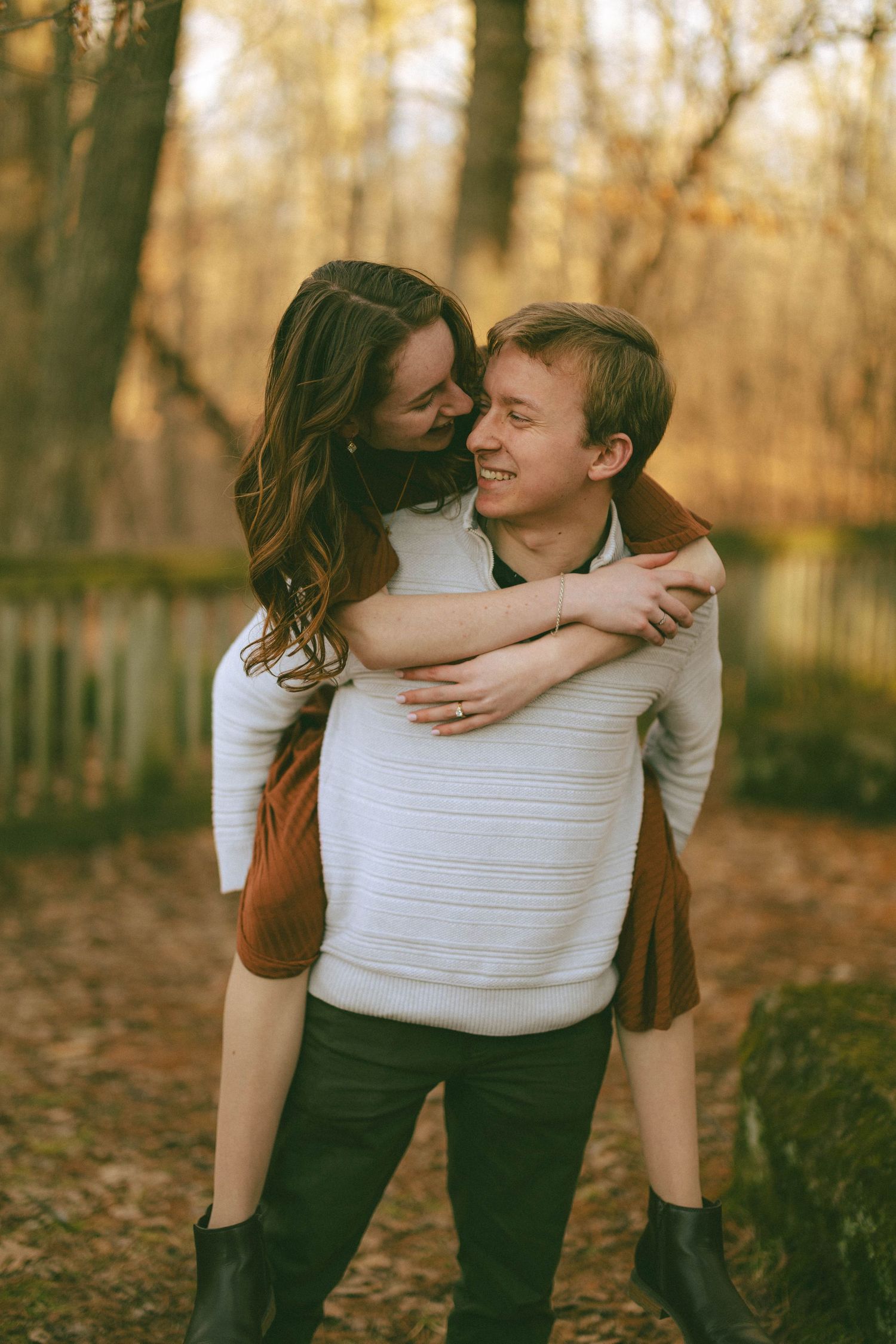 Couple sharing a piggyback ride and laughing in autumn forest setting.