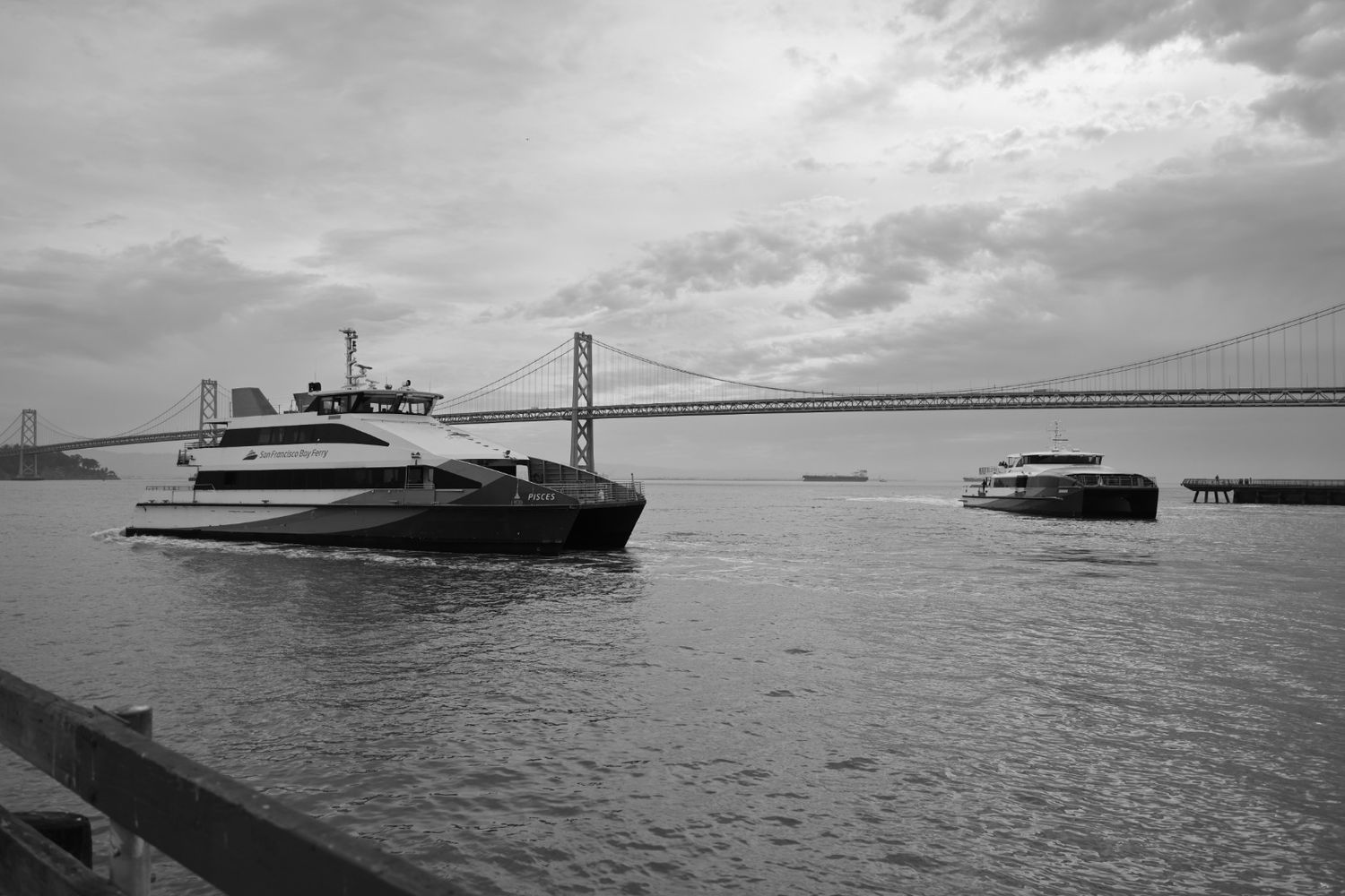 Black and white photo of ferry boats on San Francisco Bay with the Bay Bridge in the background.