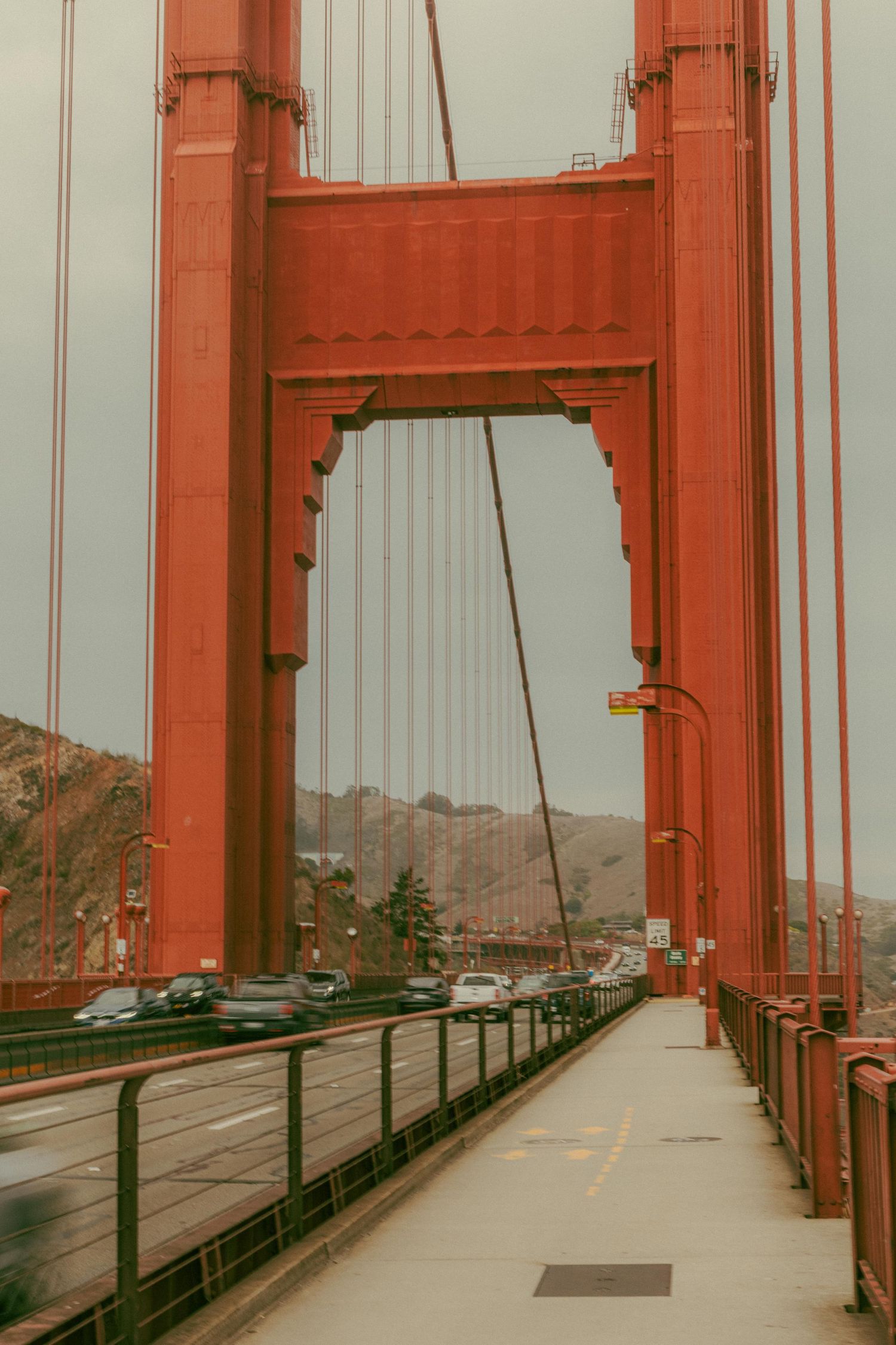Close-up view of the iconic red Golden Gate Bridge tower with cars on the roadway and pedestrian walkway.