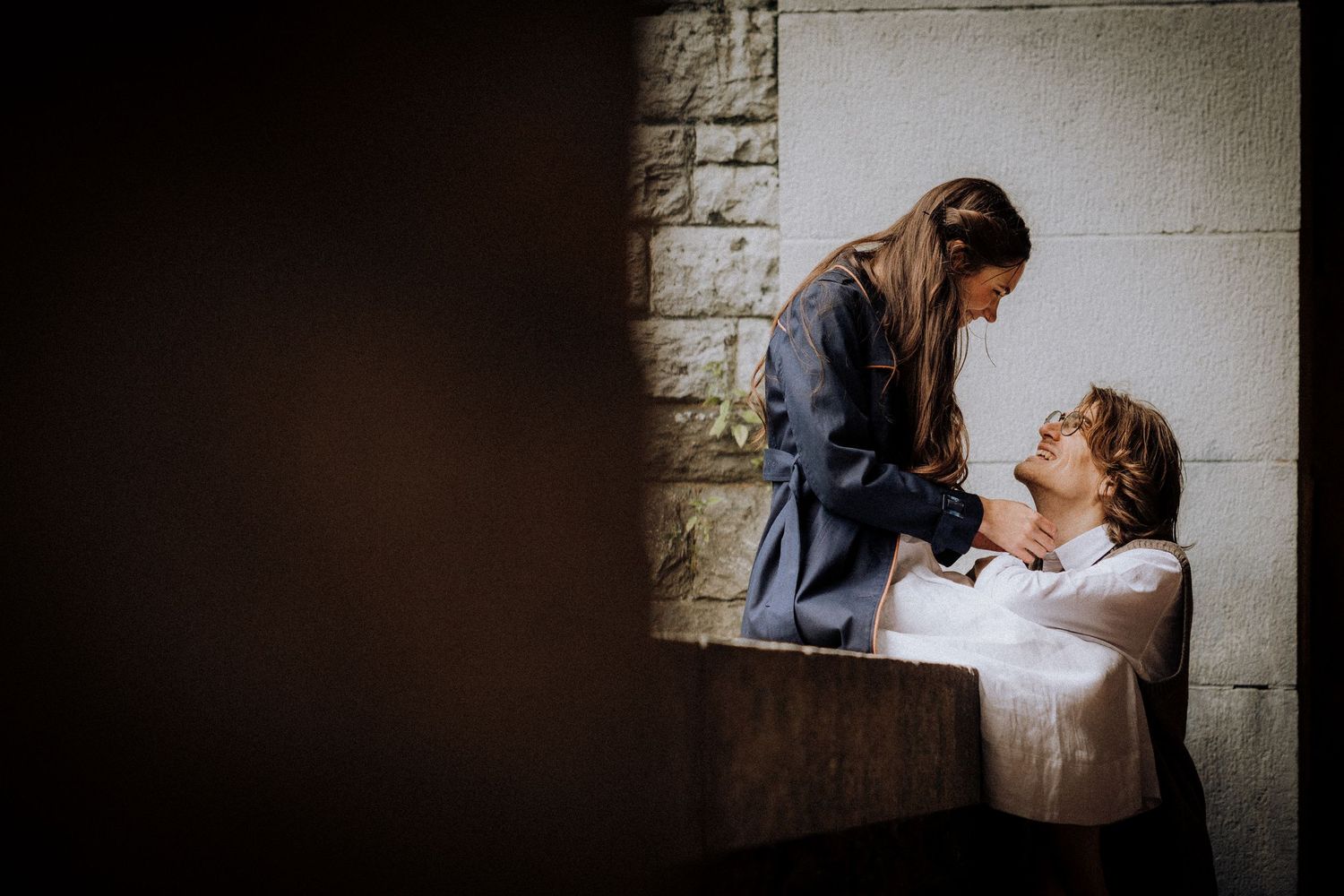 A tender moment captured between two people in dramatic lighting against a stone wall.