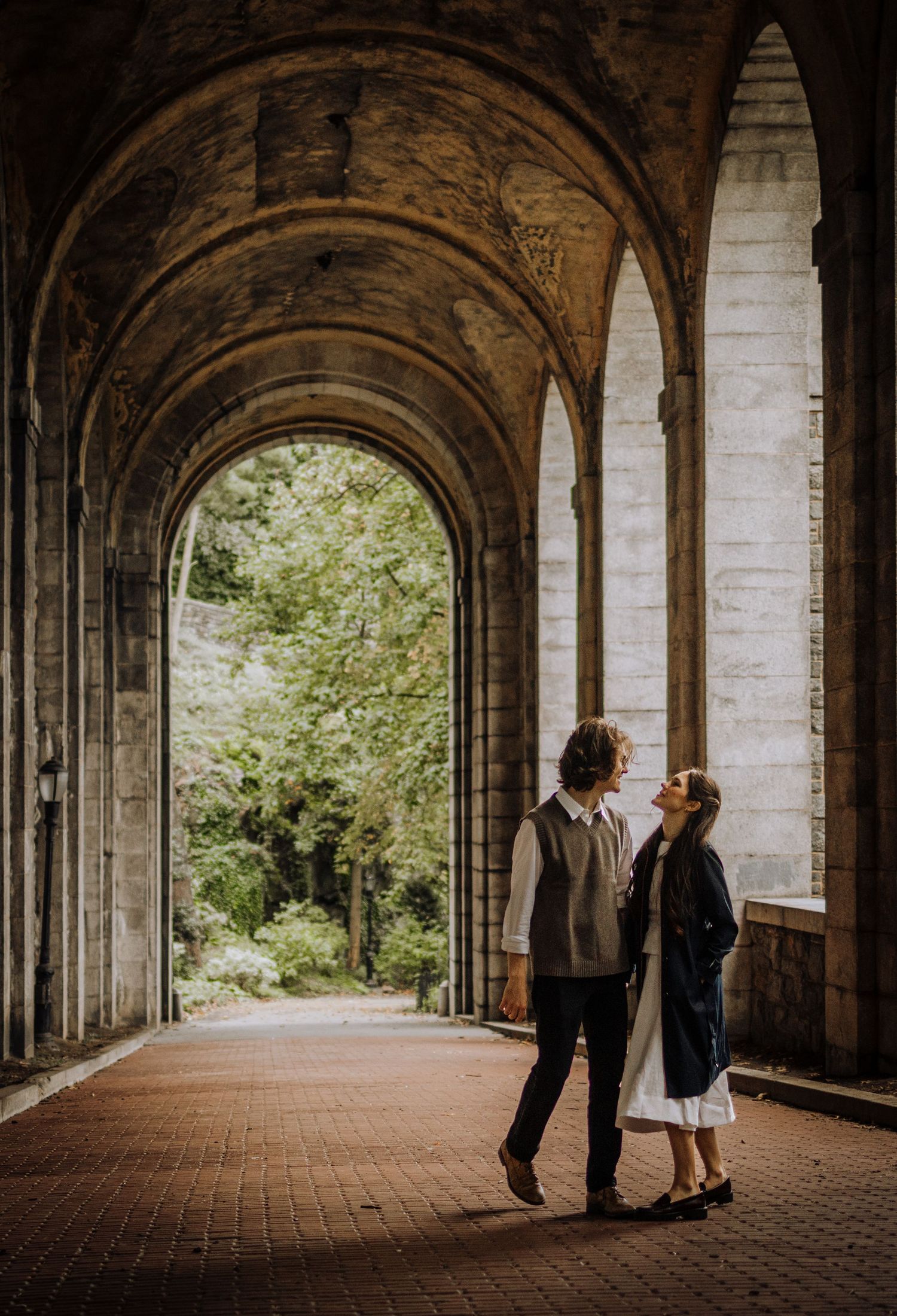 A romantic couple poses in a beautiful stone colonnade with arched ceilings.