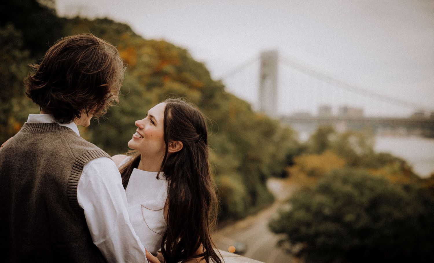 Romantic couple walking together on autumn path with city skyline in background.