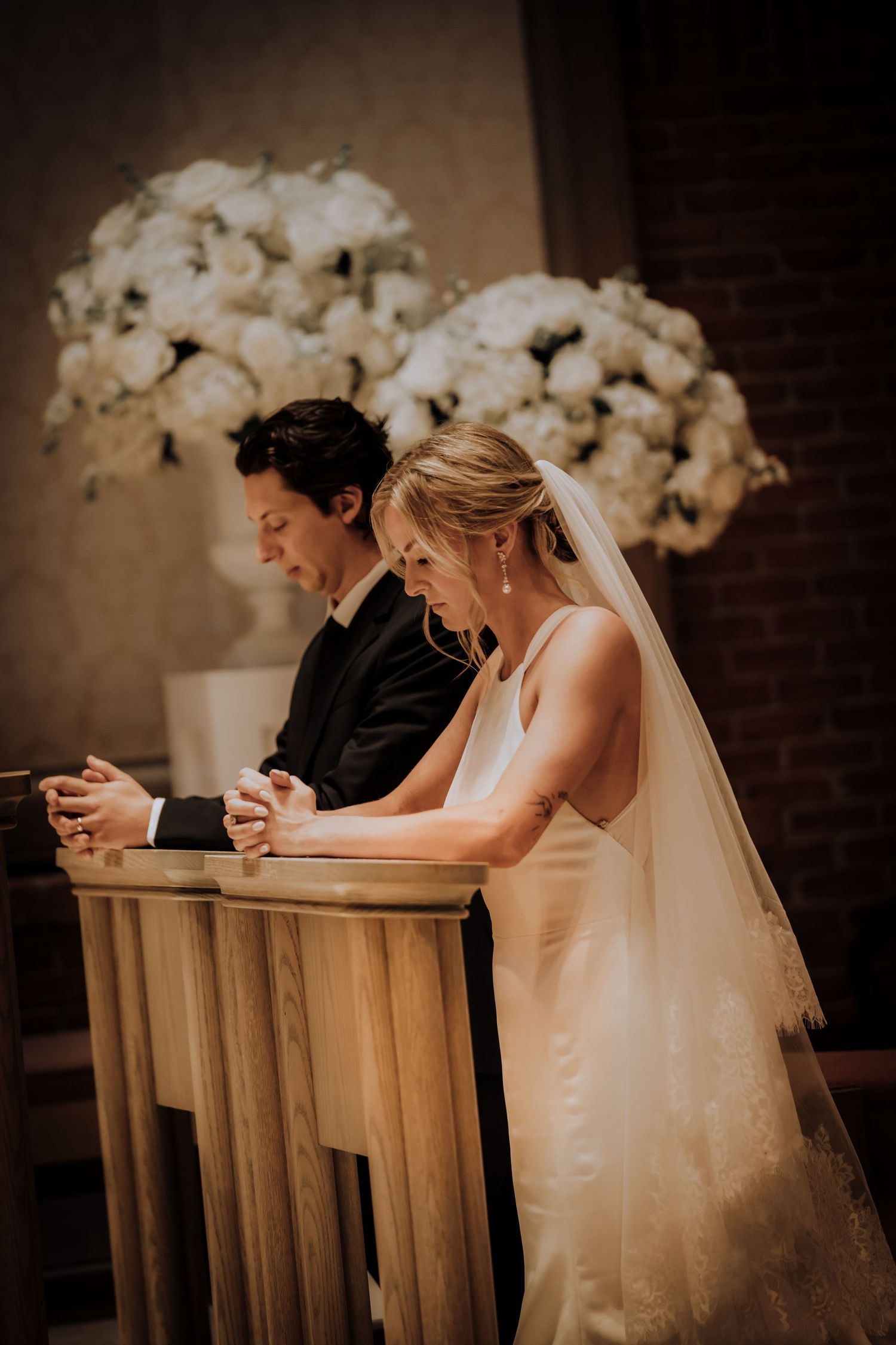 A couple checking their phones while seated at a church altar with white orchid decorations.