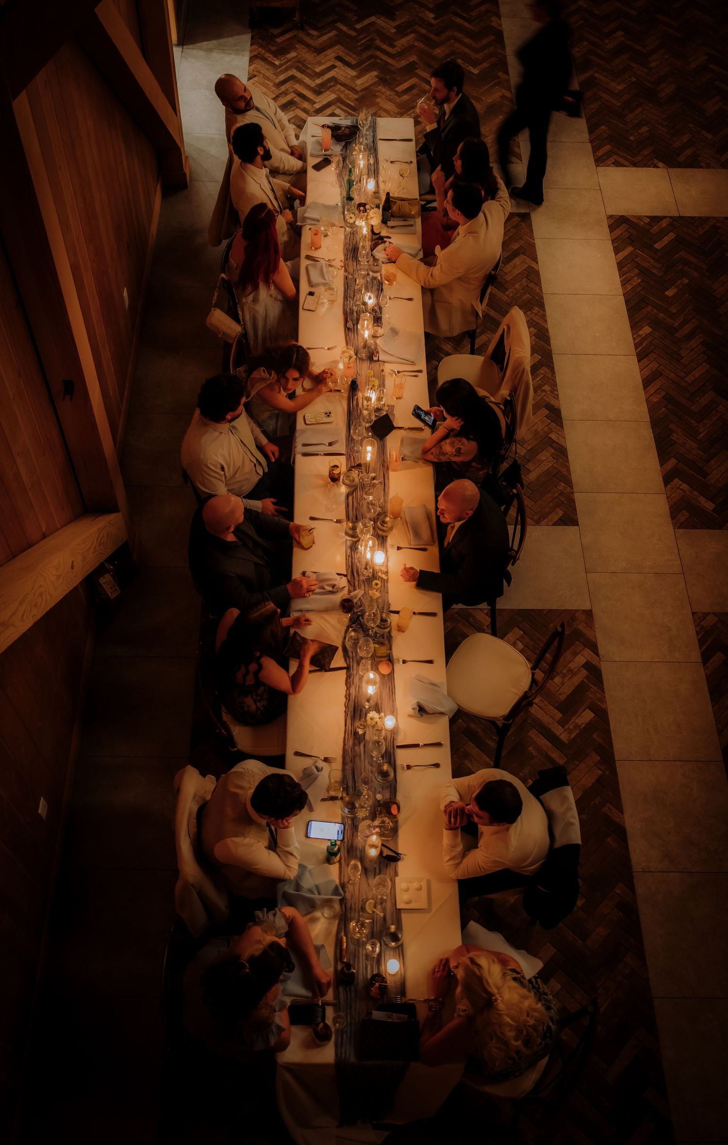 Overhead view of wedding guests dining at a long candlelit table during an evening reception.Editorial and Cinematic Wedding photos