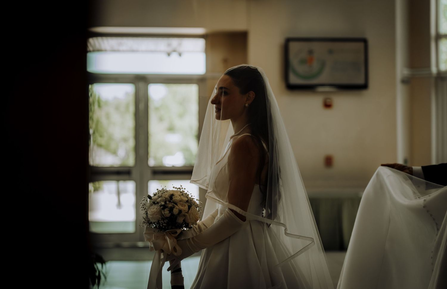 A silhouetted figure in a wedding dress stands in front of a bright window in a church.Editorial and Cinematic Wedding photos