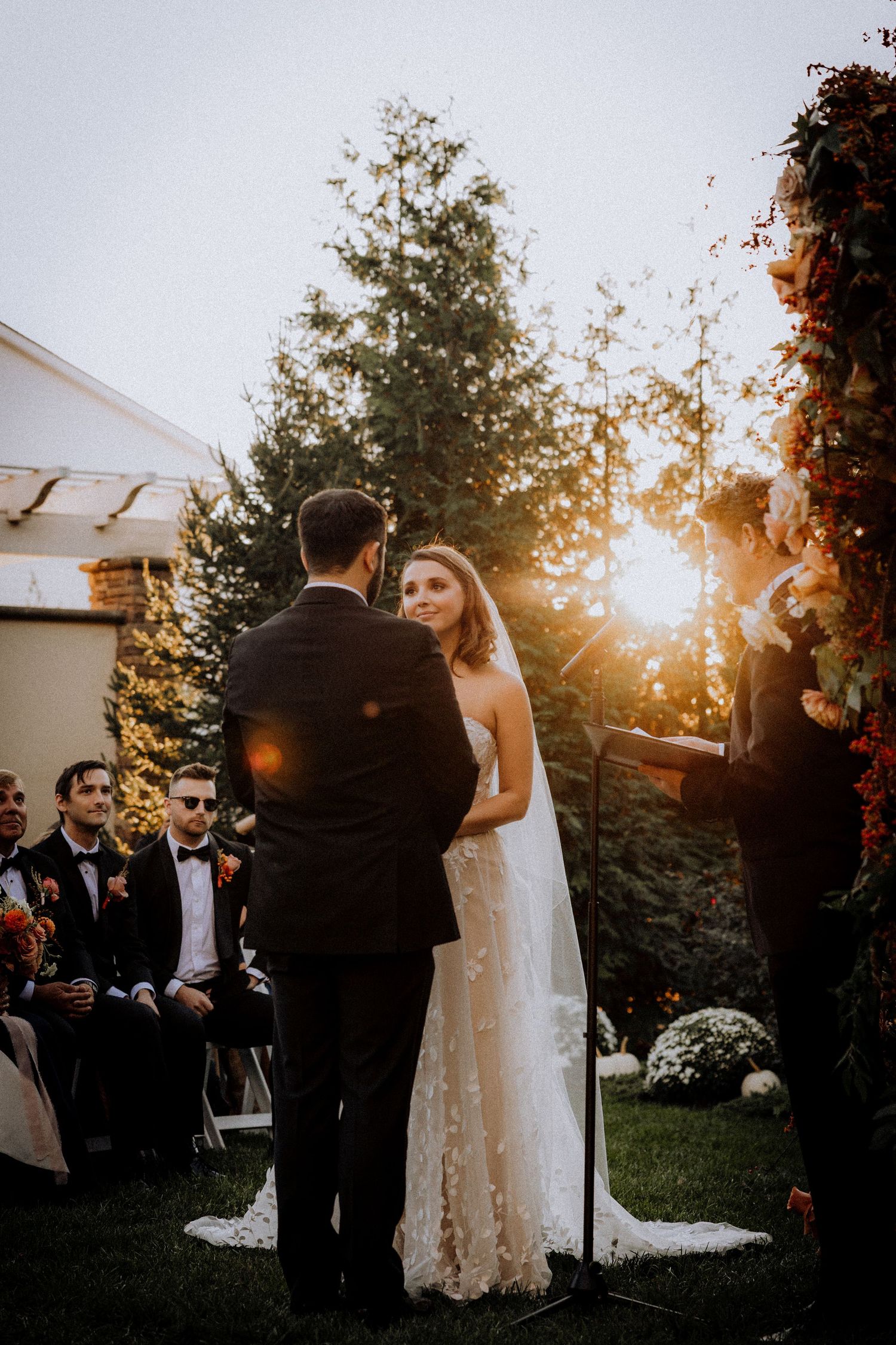 Outdoor wedding celebration during golden hour with guests mingling in a garden setting.