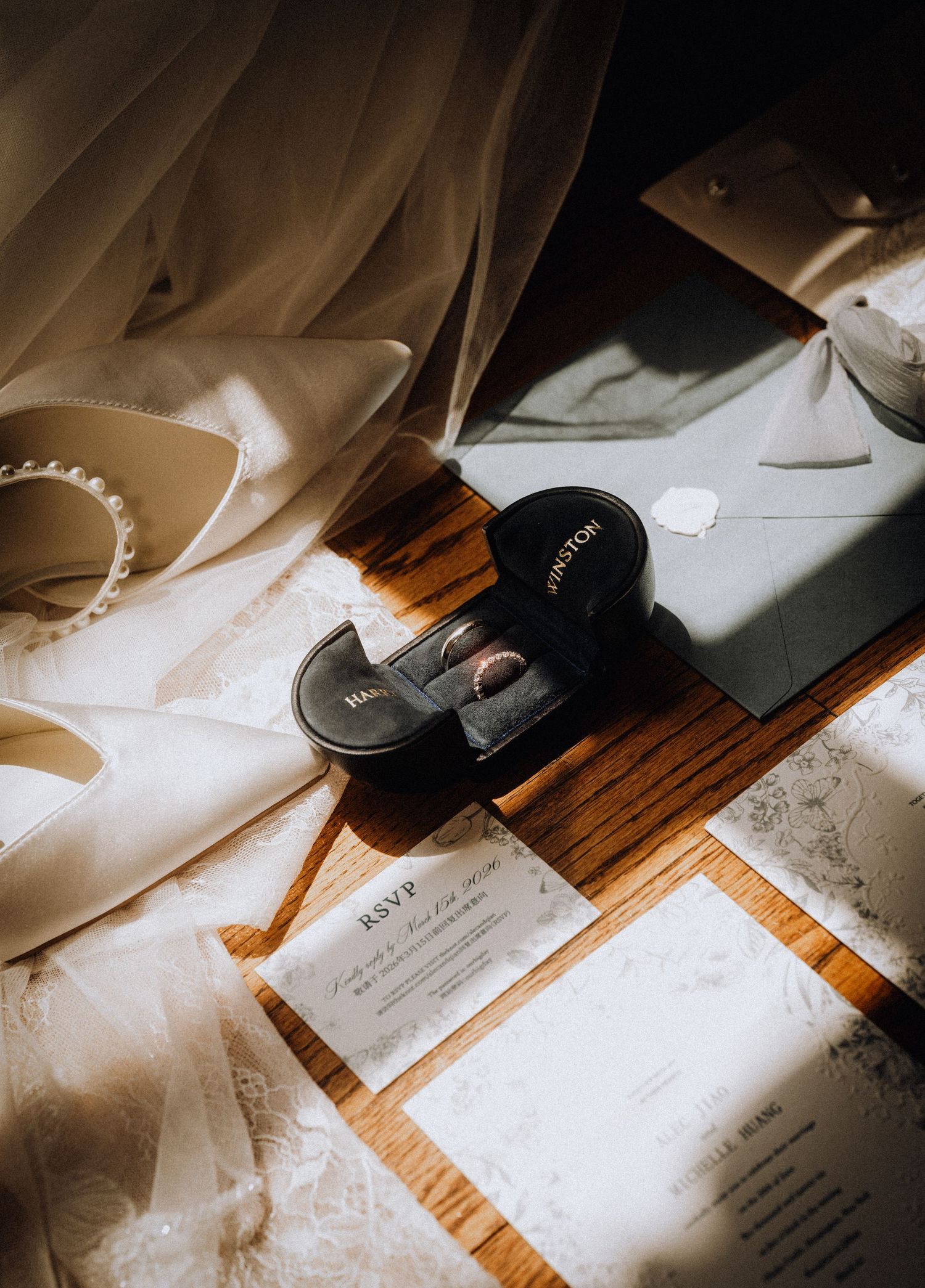 Elegant wedding flat lay with RSVP cards, pearl heels, ring box, and lace details on wooden surface.