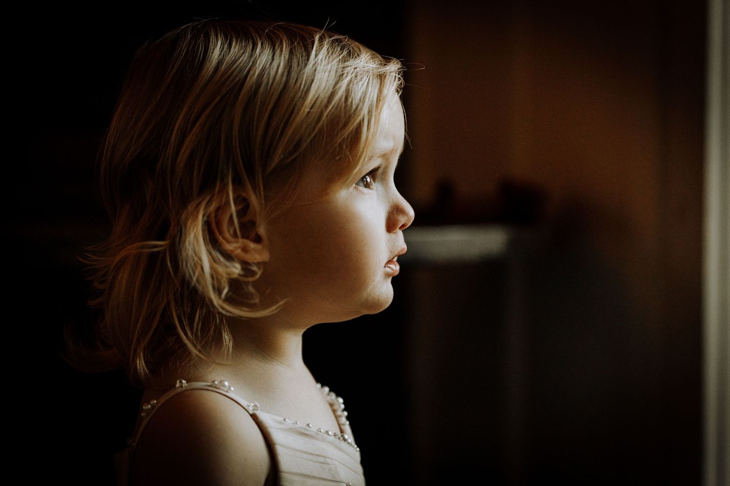 Silhouette of child looking through window in dramatic lighting.