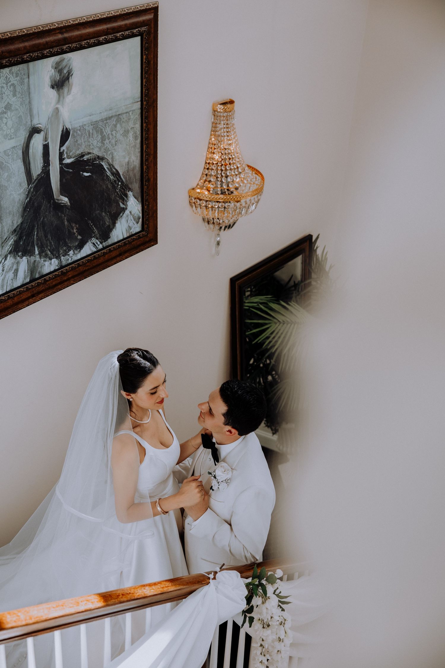 Elegant wedding photos on a staircase with framed artwork and a crystal chandelier.