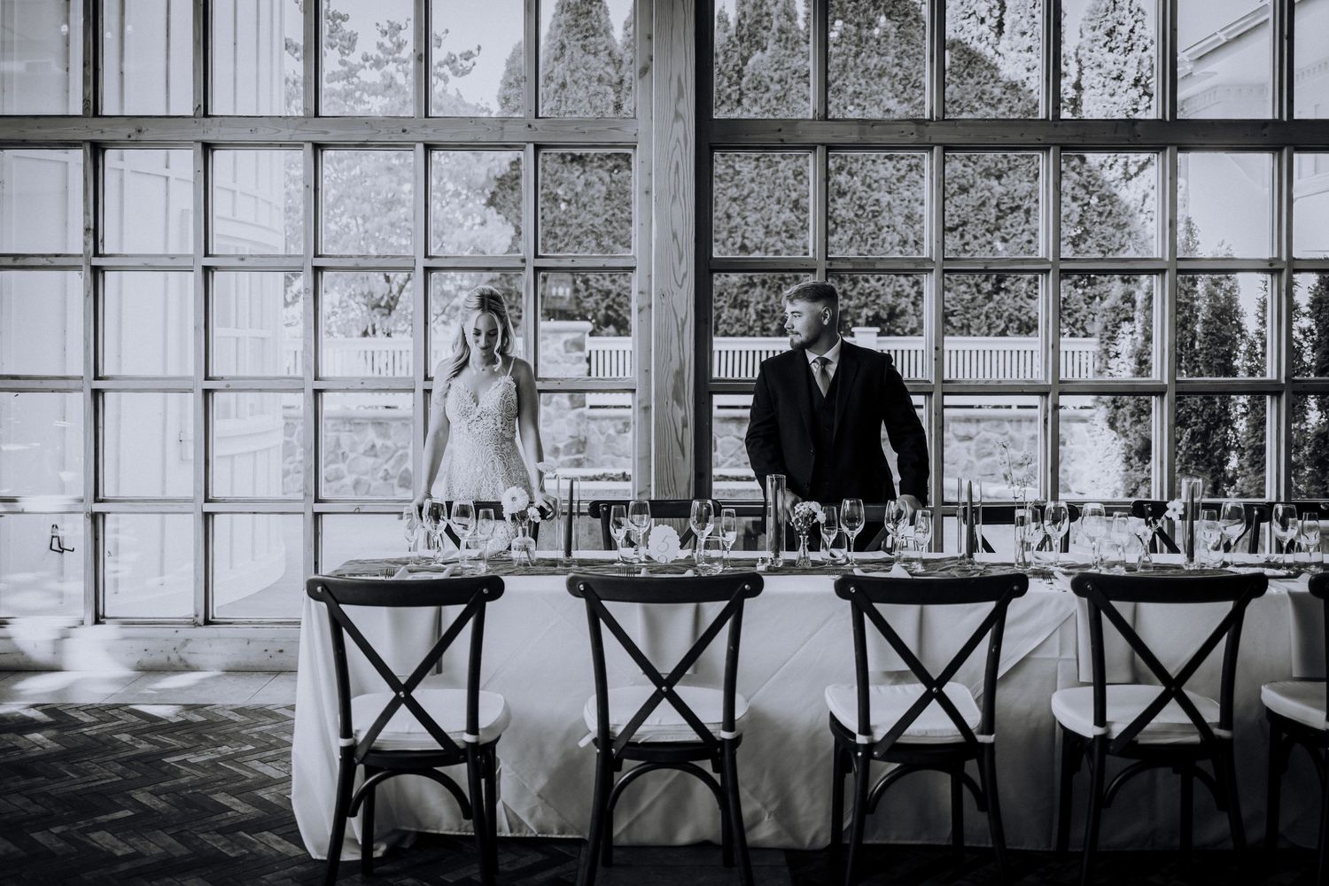 Elegant reception venue with industrial windows and cross-back chairs in moody lighting.Editorial and Cinematic Wedding photos