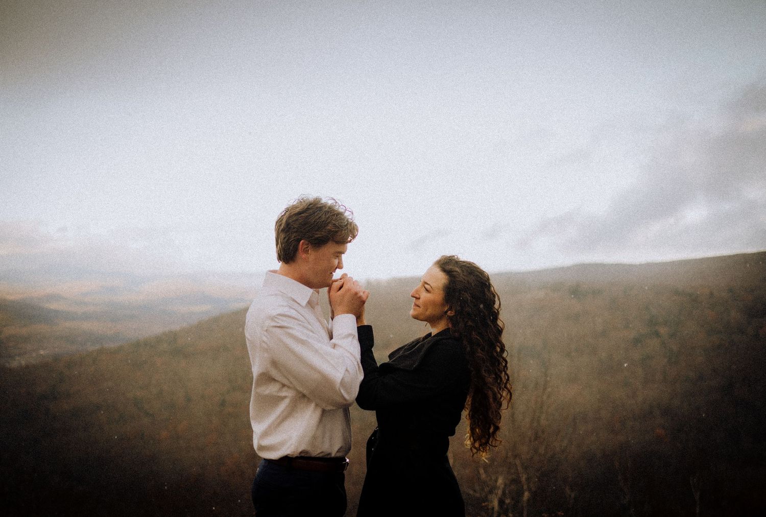 Couple embracing against a scenic mountain landscape during golden hour.