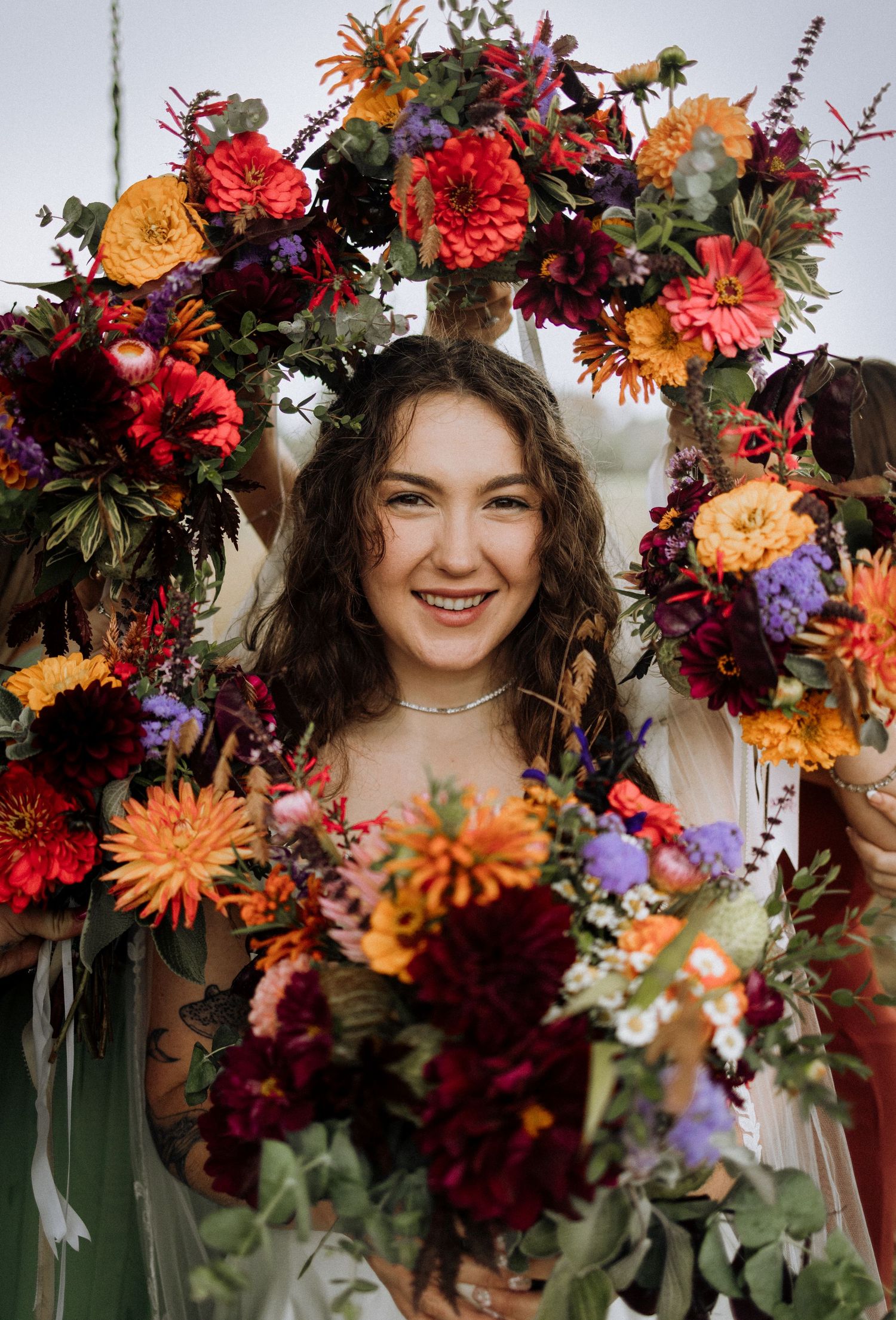 A stunning fall floral crown features vibrant red, orange, and purple blooms with lush greenery.