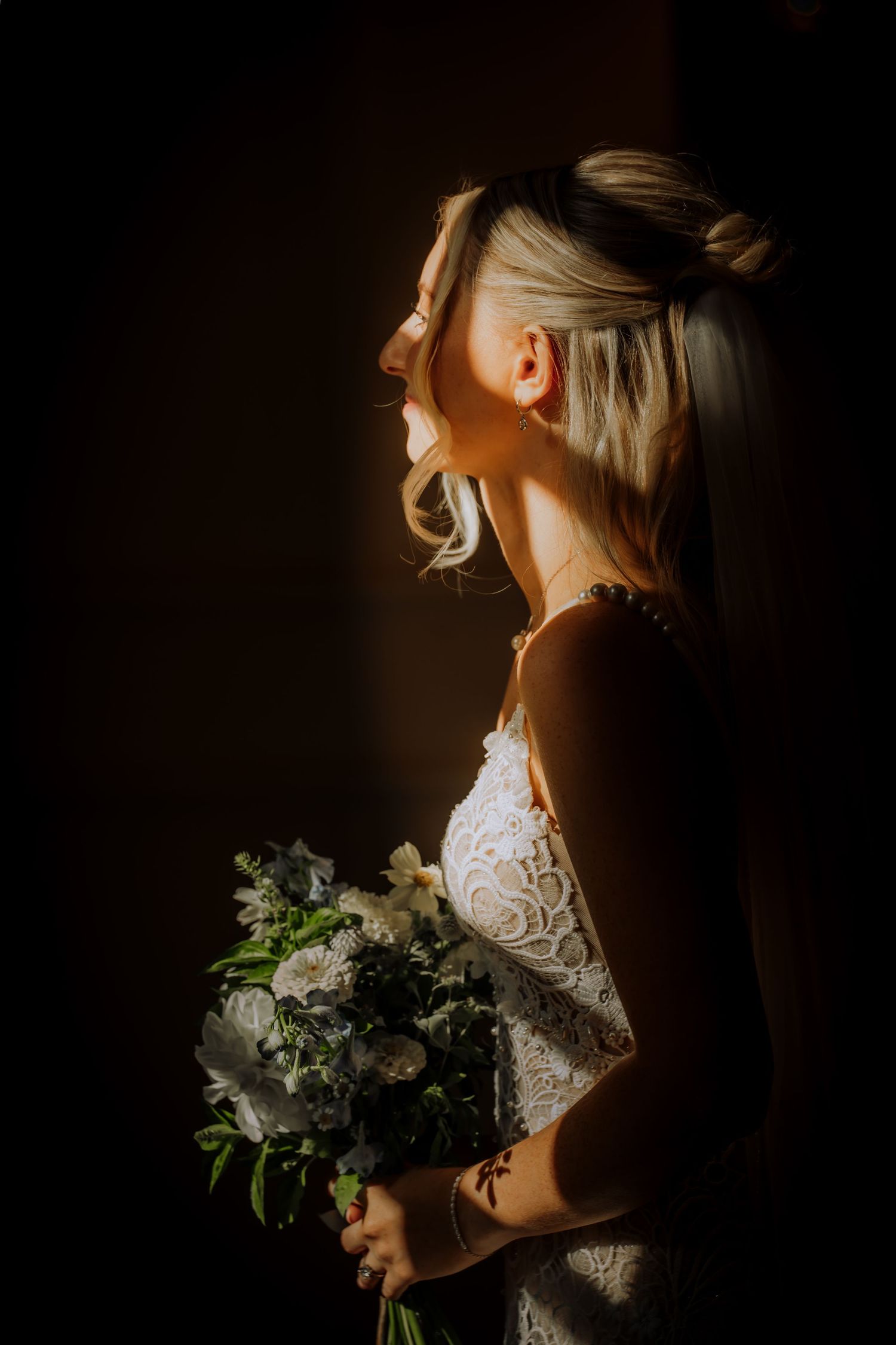 Dramatic side-lit portrait with white lace dress and floral bouquet.Editorial and Cinematic Wedding photos