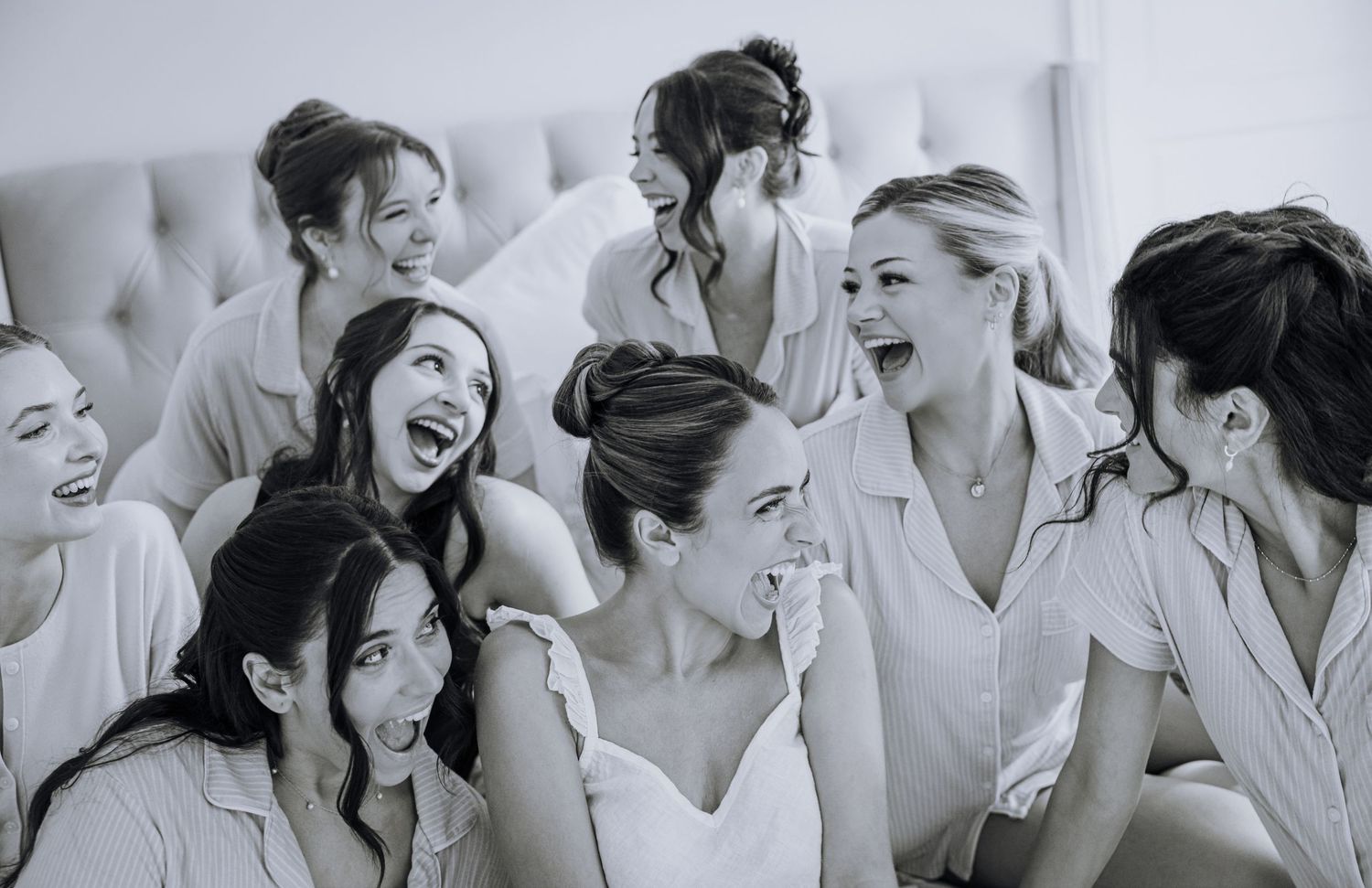 Black and white photo of a bride laughing with her bridesmaids in matching pajamas during wedding preparations.