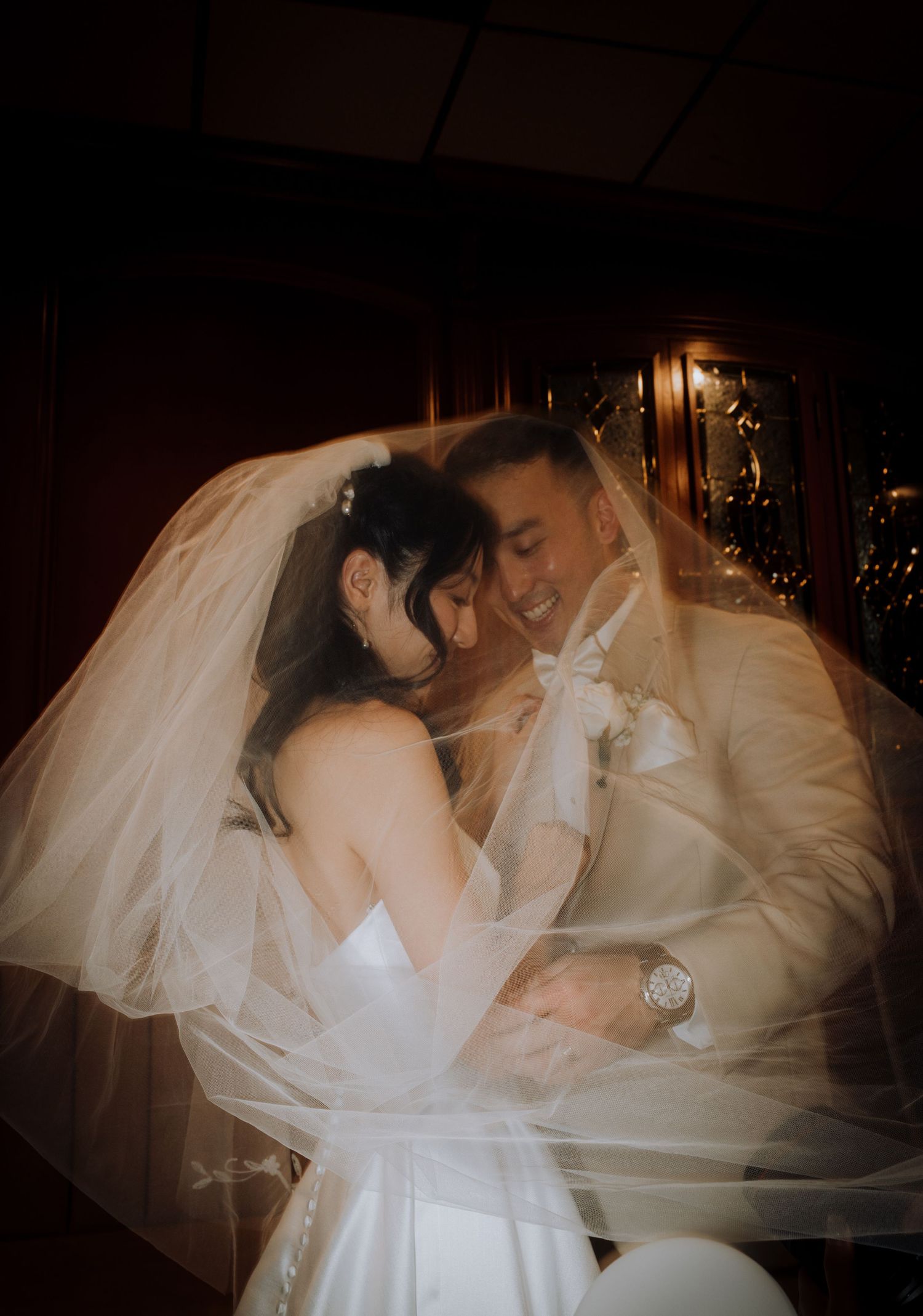 Romantic low-light wedding portraits with flowing veil creating dreamy atmosphere.